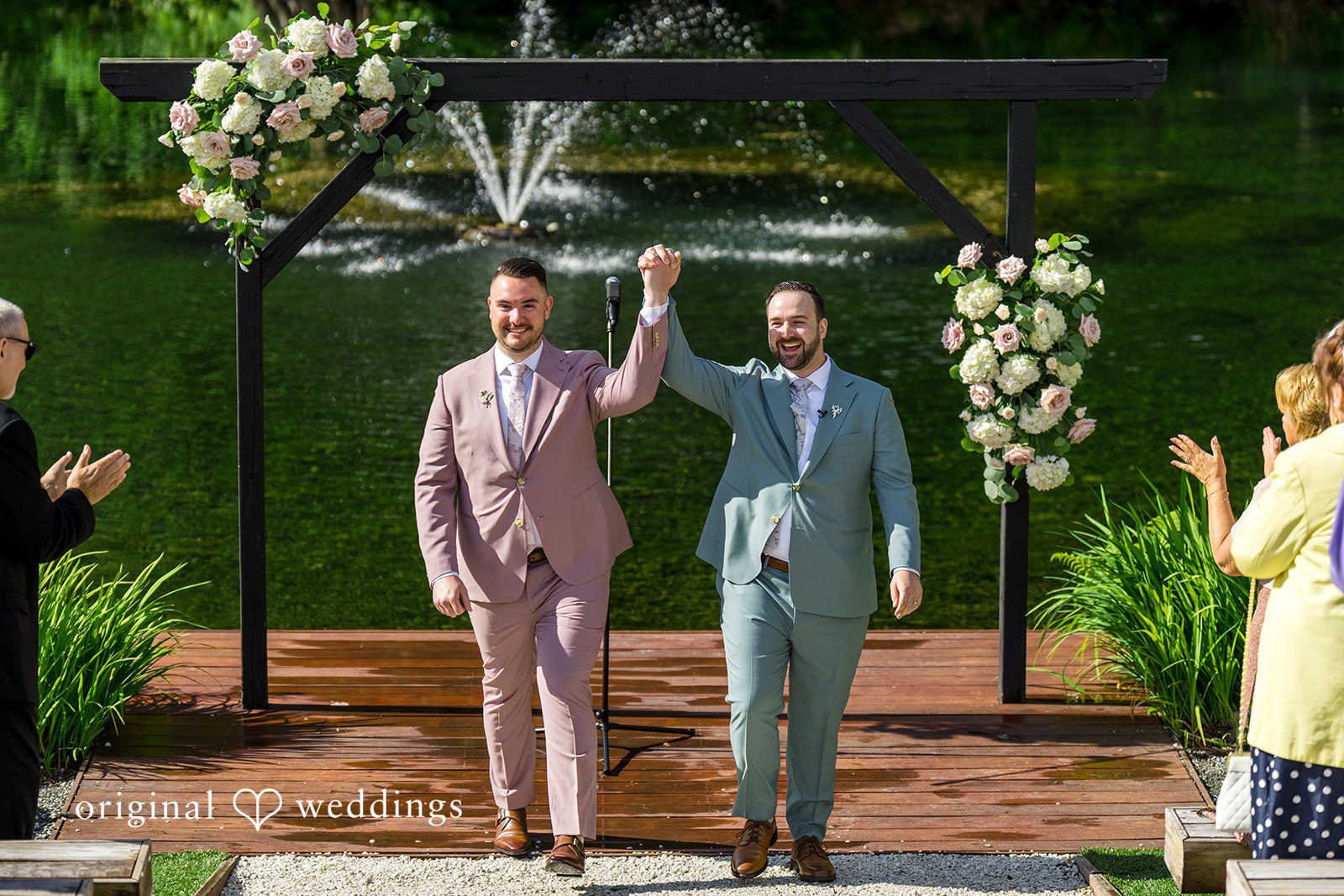 Kristian + Jeff Couple smiling and raising their hands together in celebration at the end of their wedding ceremony.