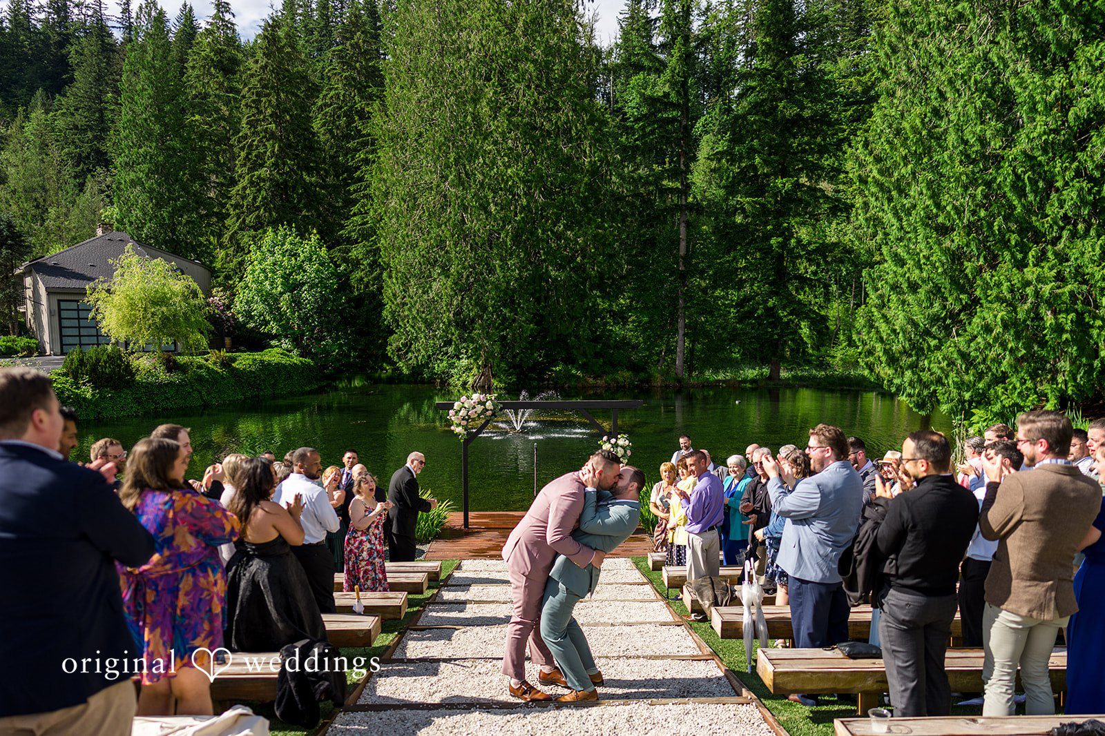 Kristian + Jeff Couple walking down a stone aisle while wedding guests applaud on both sides.