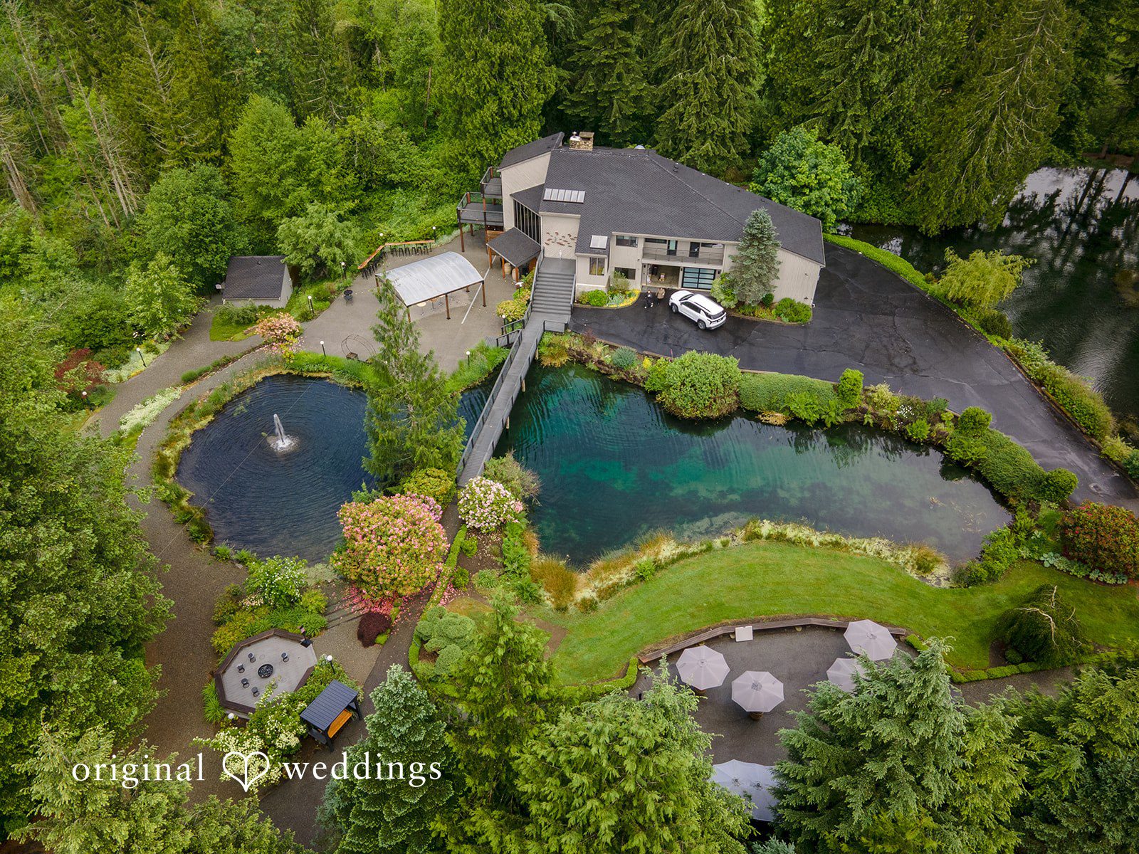 Kristian + Jeff Aerial view of a large estate featuring a house, a pond, lush green lawns, and surrounding trees.