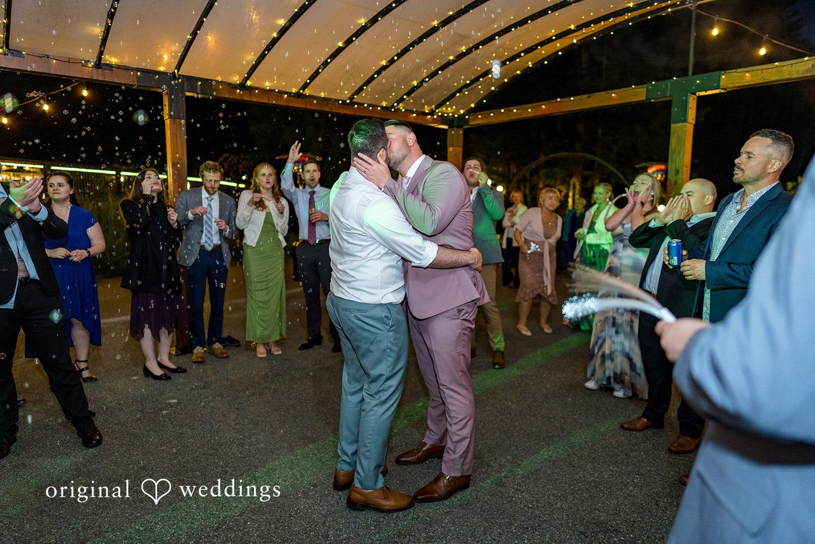 Kristian + Jeff Couple sharing a kiss on the dance floor surrounded by wedding guests at night.