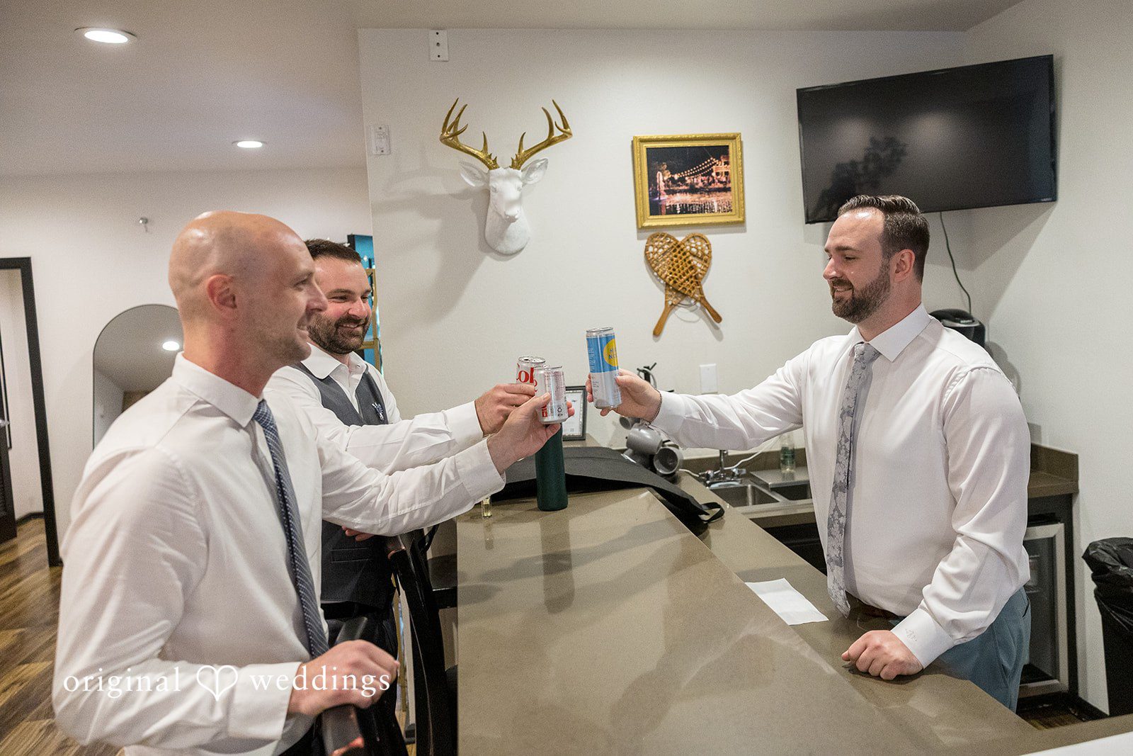 Kristian + Jeff Two men wearing white shirts and ties smiling and interacting behind a counter or bar.