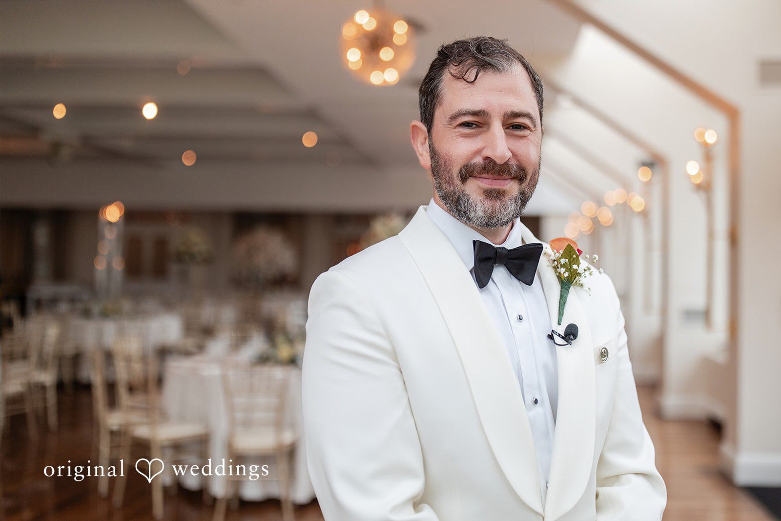 Portrait of a groom wearing a white tuxedo and a black bowtie.