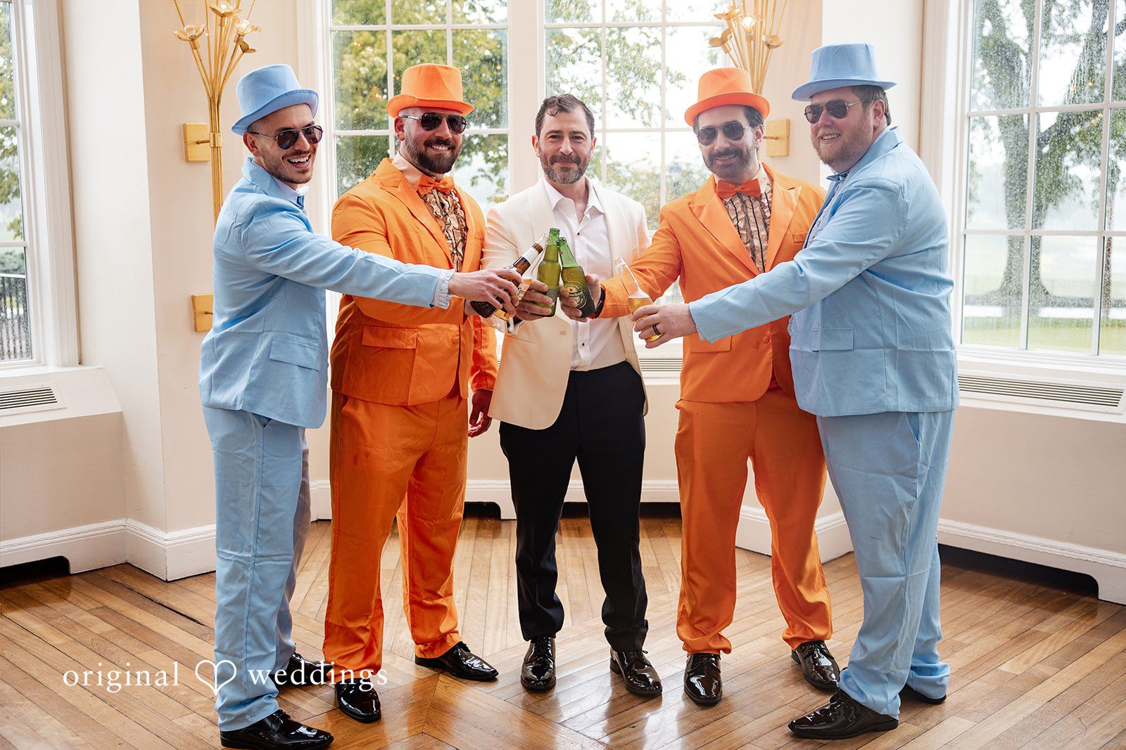 Groom posing playfully with friends wearing colorful blue and orange suits.