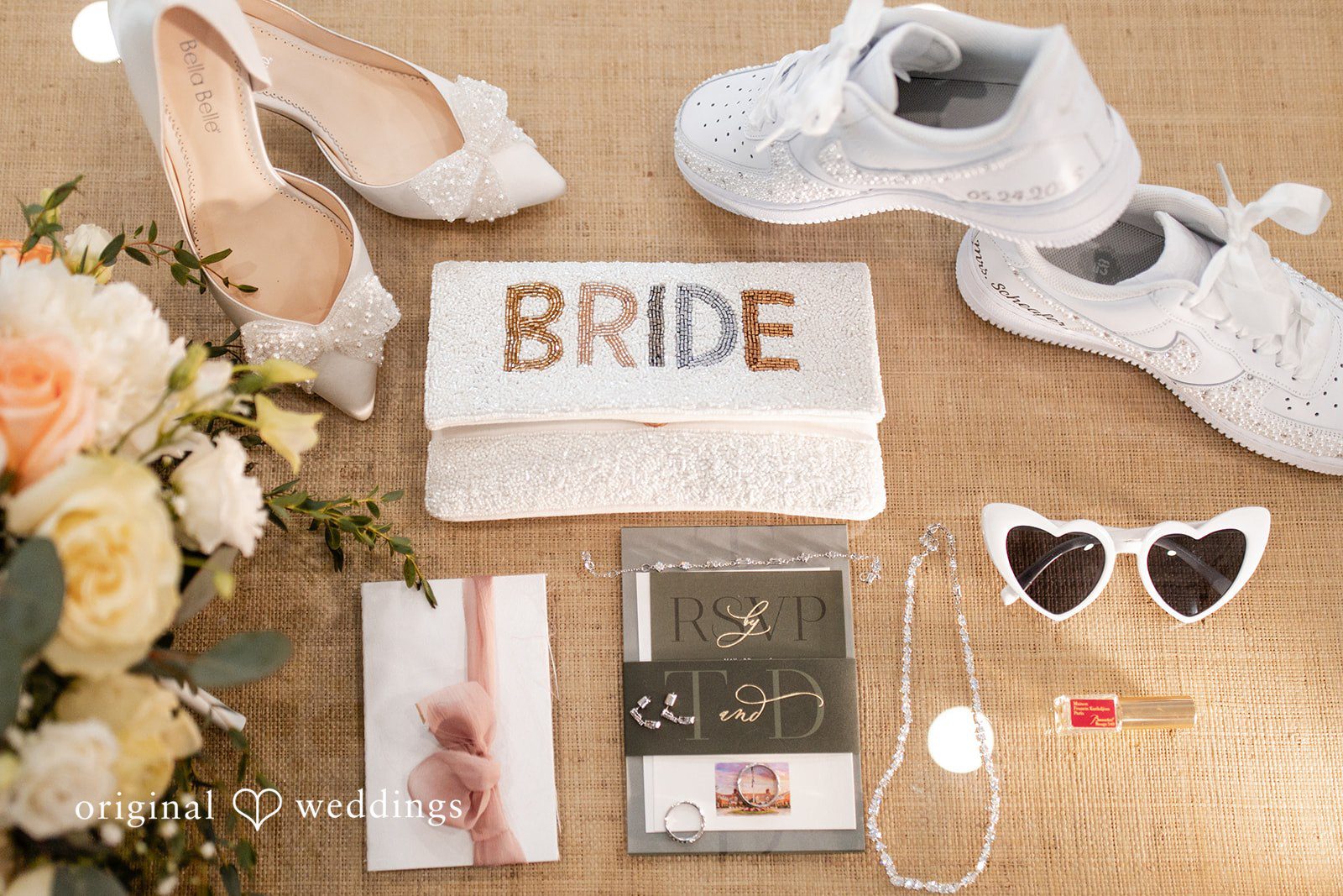 Wedding flat lay featuring bridal sneakers, sunglasses, a clutch, and floral details.