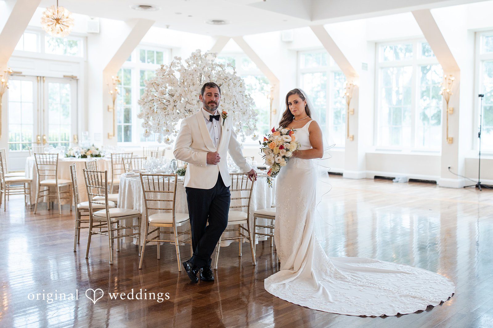 Bride and groom posing in the middle of an empty, elegant reception hall.