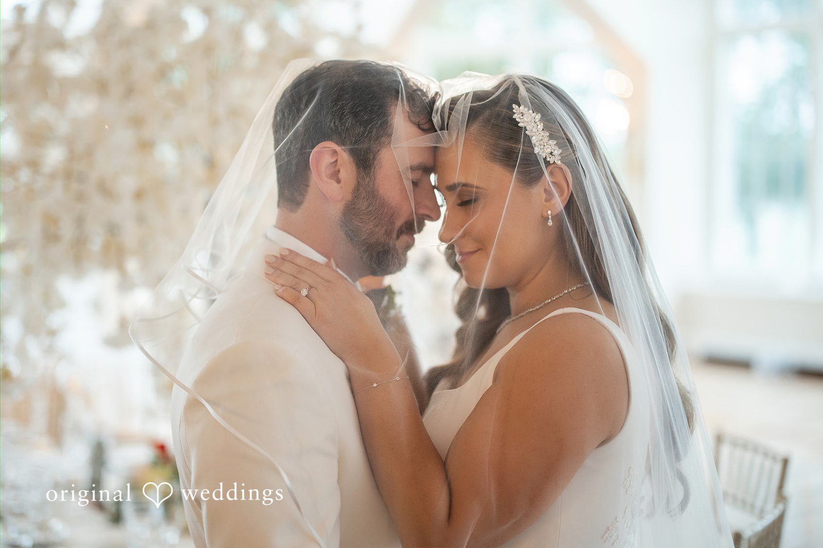 Bride and groom sharing an intimate moment with their foreheads touching under a veil.