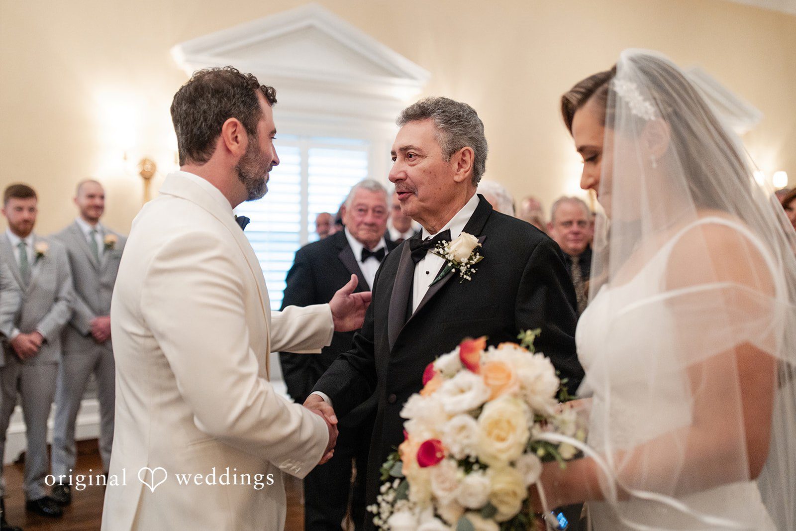 Groom and a wedding guest speaking with the bride visible on the right.
