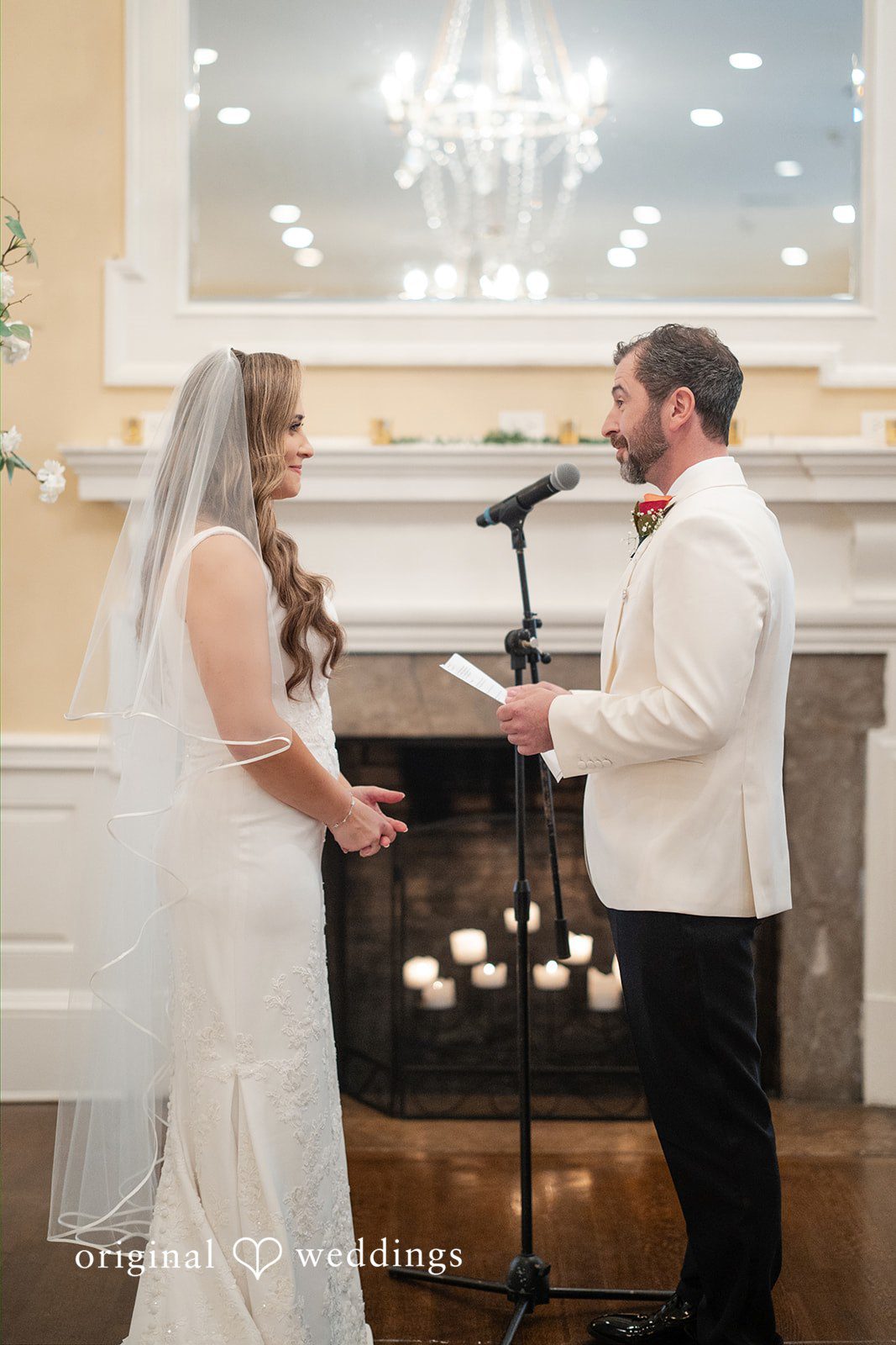 Bride and groom facing each other and exchanging vows in front of a fireplace during their wedding ceremony.