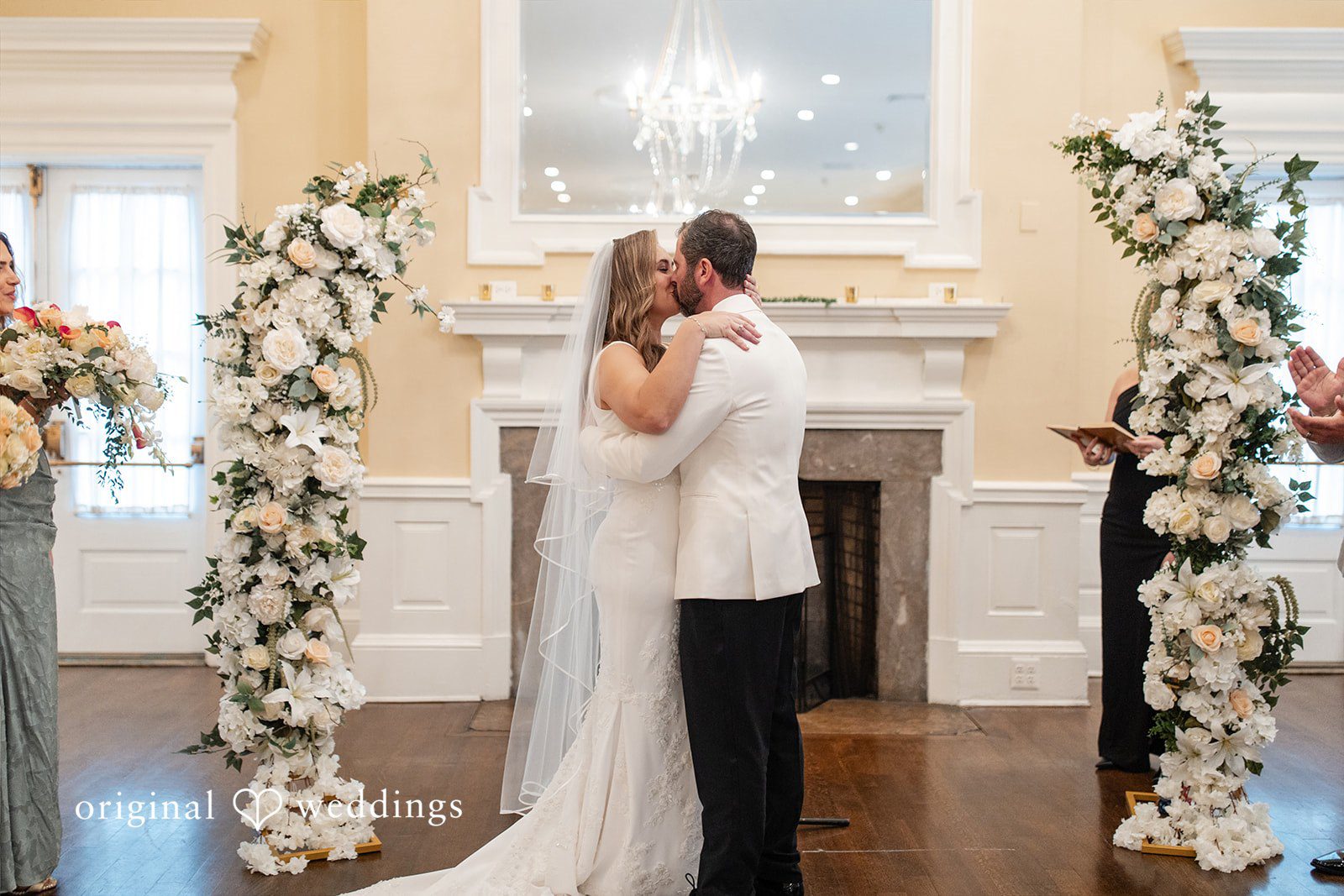 Bride and groom kissing beneath a white floral archway.