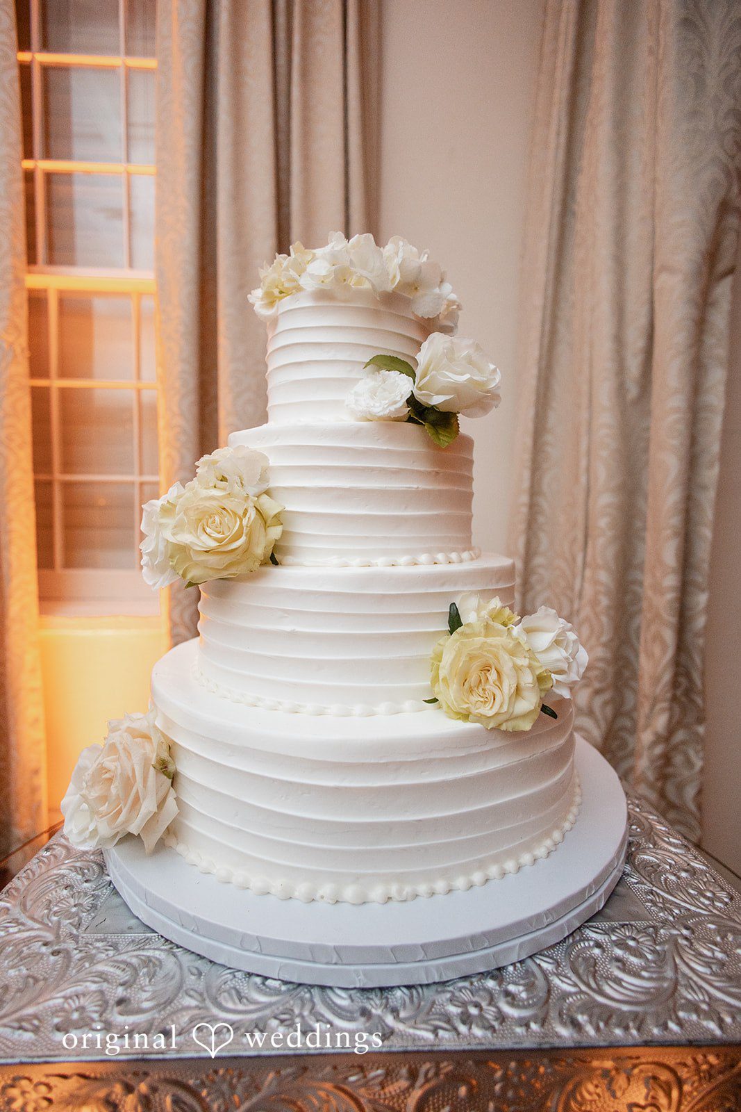 Three-tiered white wedding cake decorated with delicate floral patterns.