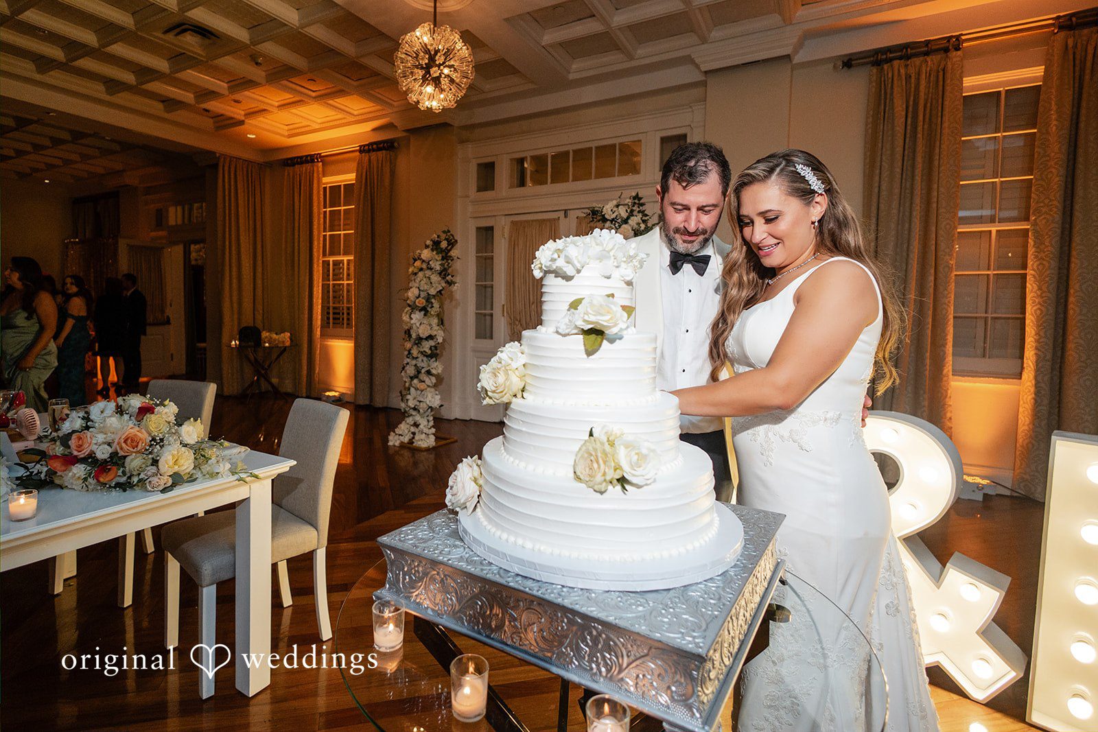 Bride and groom smiling as they prepare to cut their multi-tiered wedding cake.