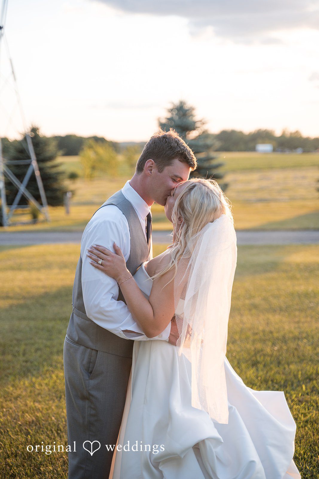 Cassandra + Adam Bride and groom embracing tightly in an open grassy field during sunset.