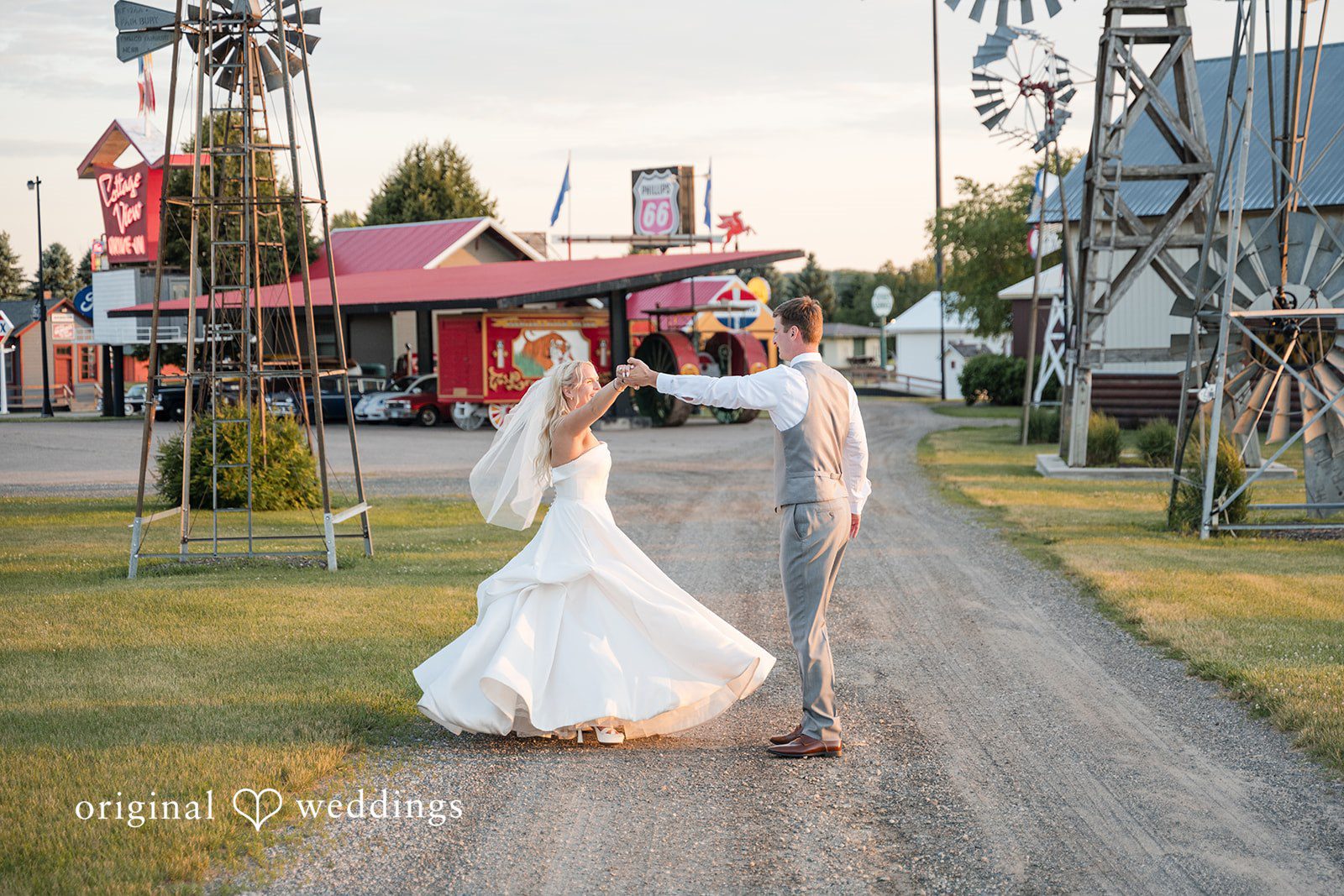 Cassandra + Adam Wide shot of the bride and groom posing on a paved path near a barn.