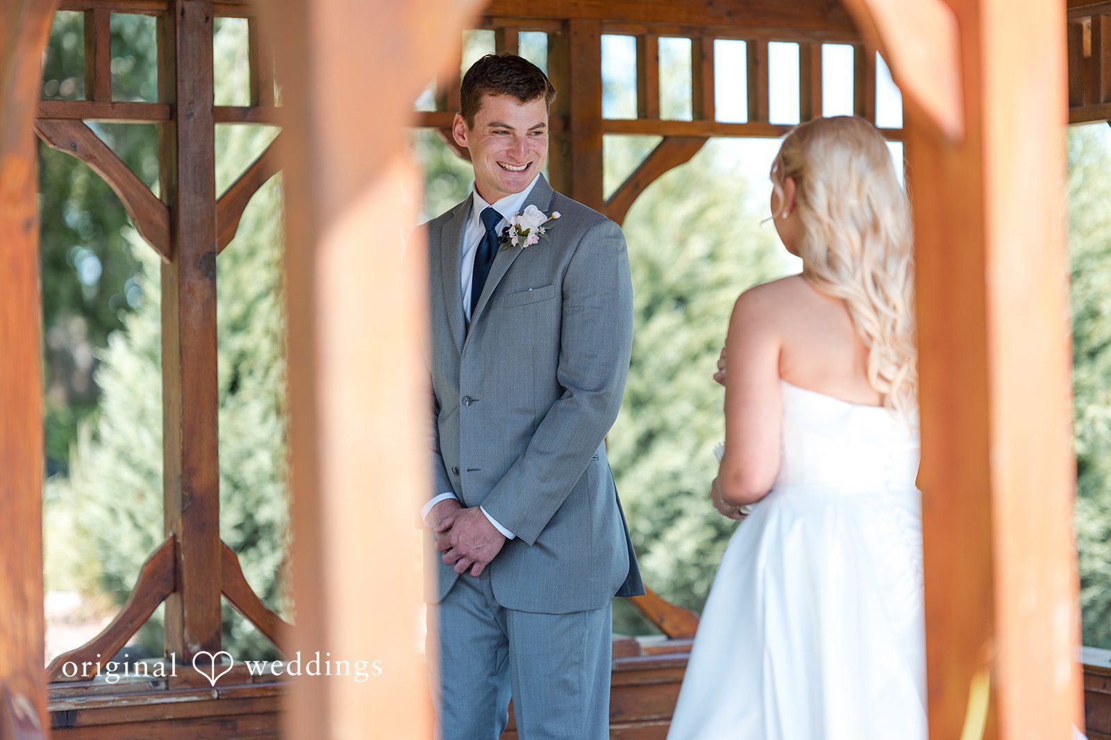 Cassandra + Adam Bride and groom standing together looking at each other under a pavilion.