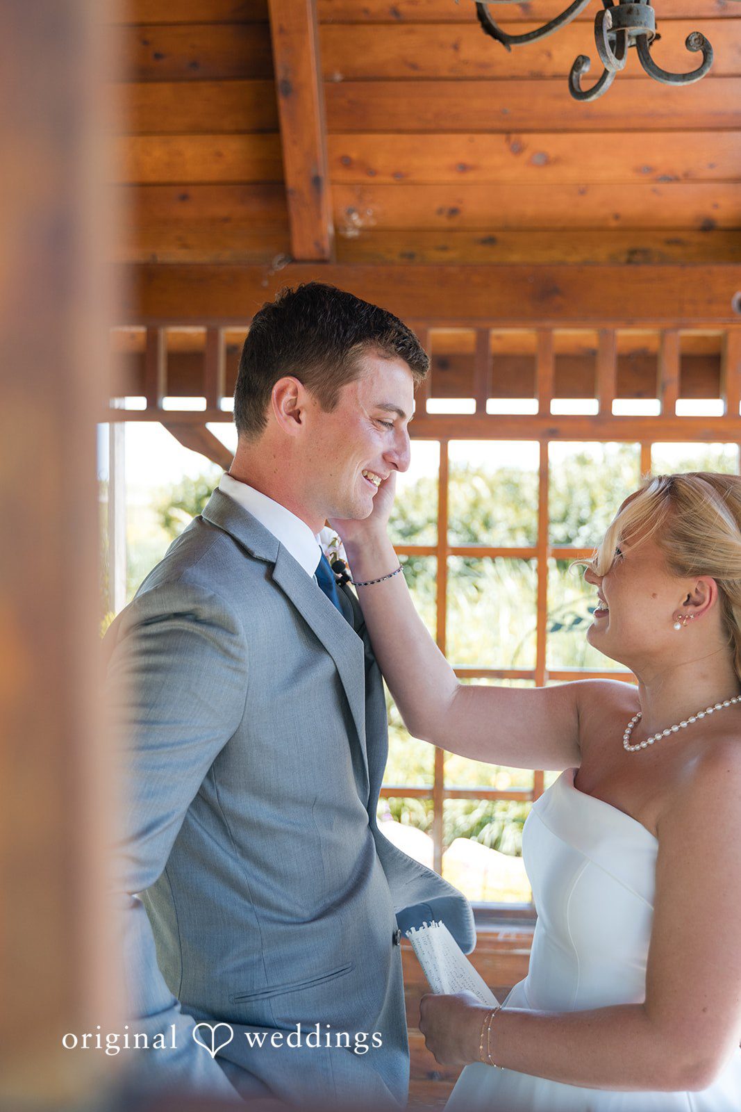 Cassandra + Adam Bride smiling and adjusting the collar of the groom's grey suit jacket.