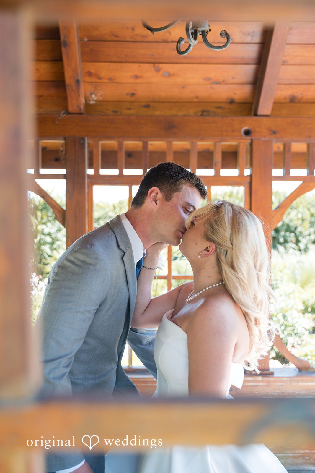 Cassandra + Adam Bride and groom sharing a close kiss inside a wooden pavilion.