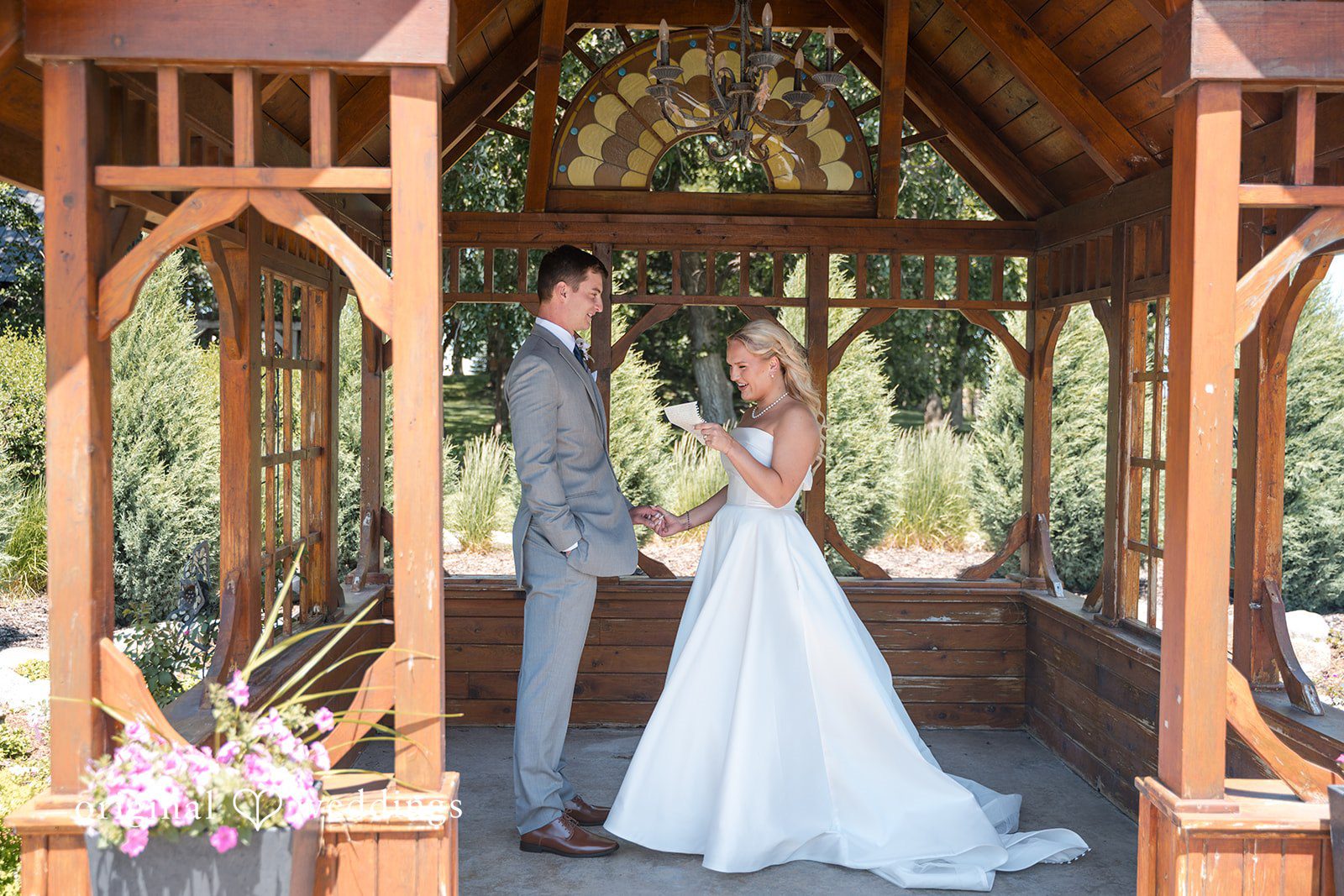 Cassandra + Adam Wide shot of the bride and groom standing together inside a large wooden gazebo.