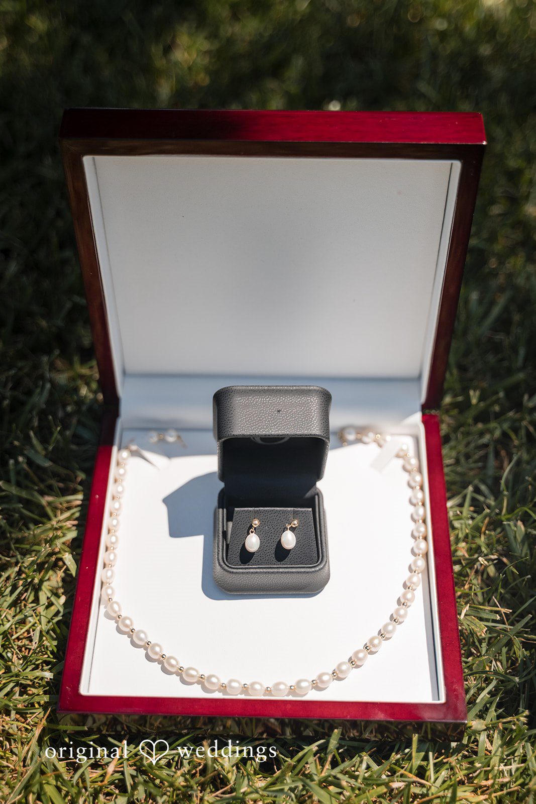 Cassandra + Adam Open wedding bos displaying accessories on a red fabric surface.