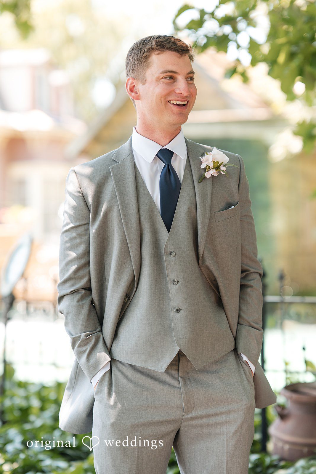 Cassandra + Adam Groom in a grey three-piece suit smiling and posing in front of trees.