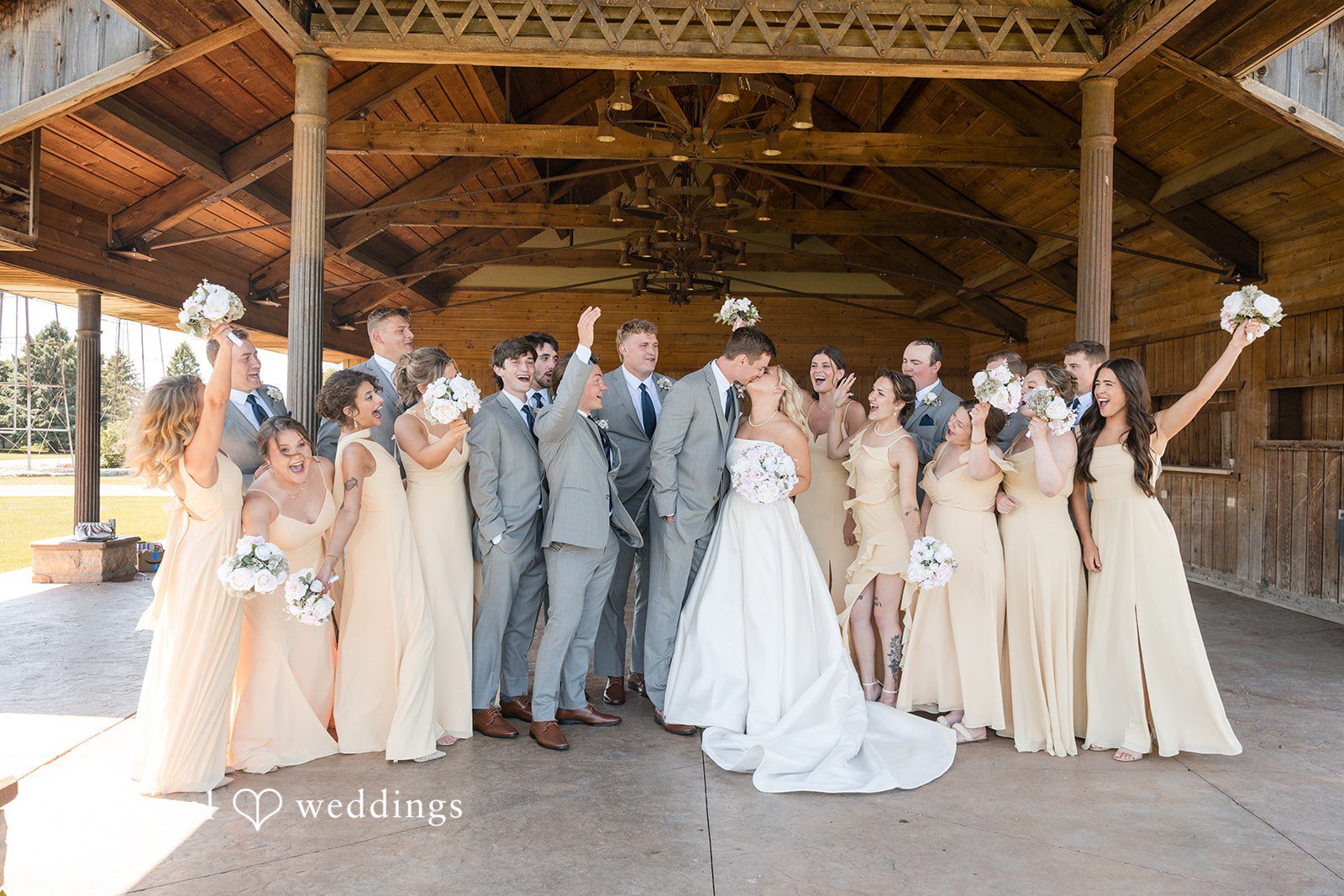 Cassandra + Adam Full wedding party posing together with raised hands inside a wooden barn.