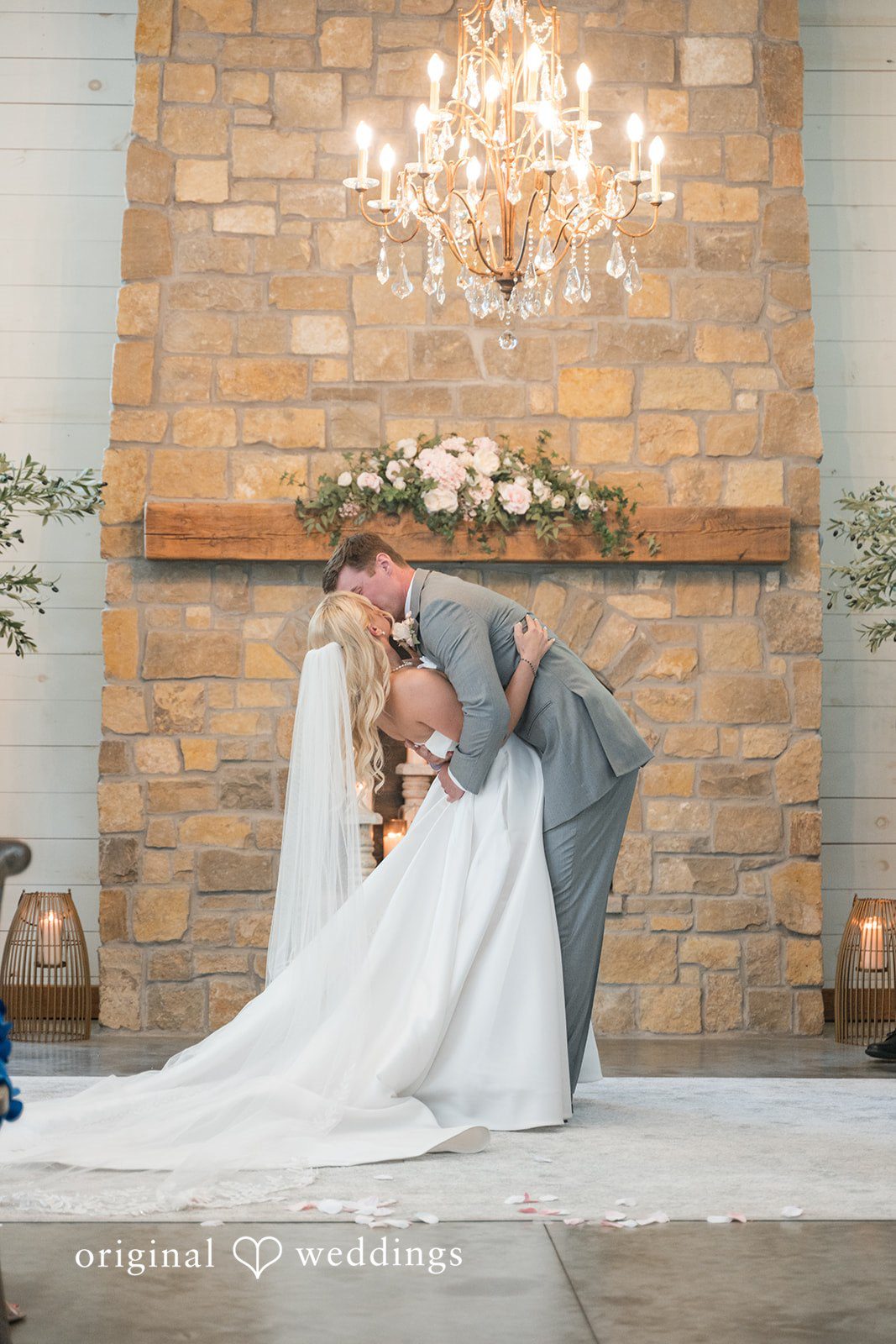 Cassandra + Adam Bride and groom dipping and kissing in front of a stone fireplace.