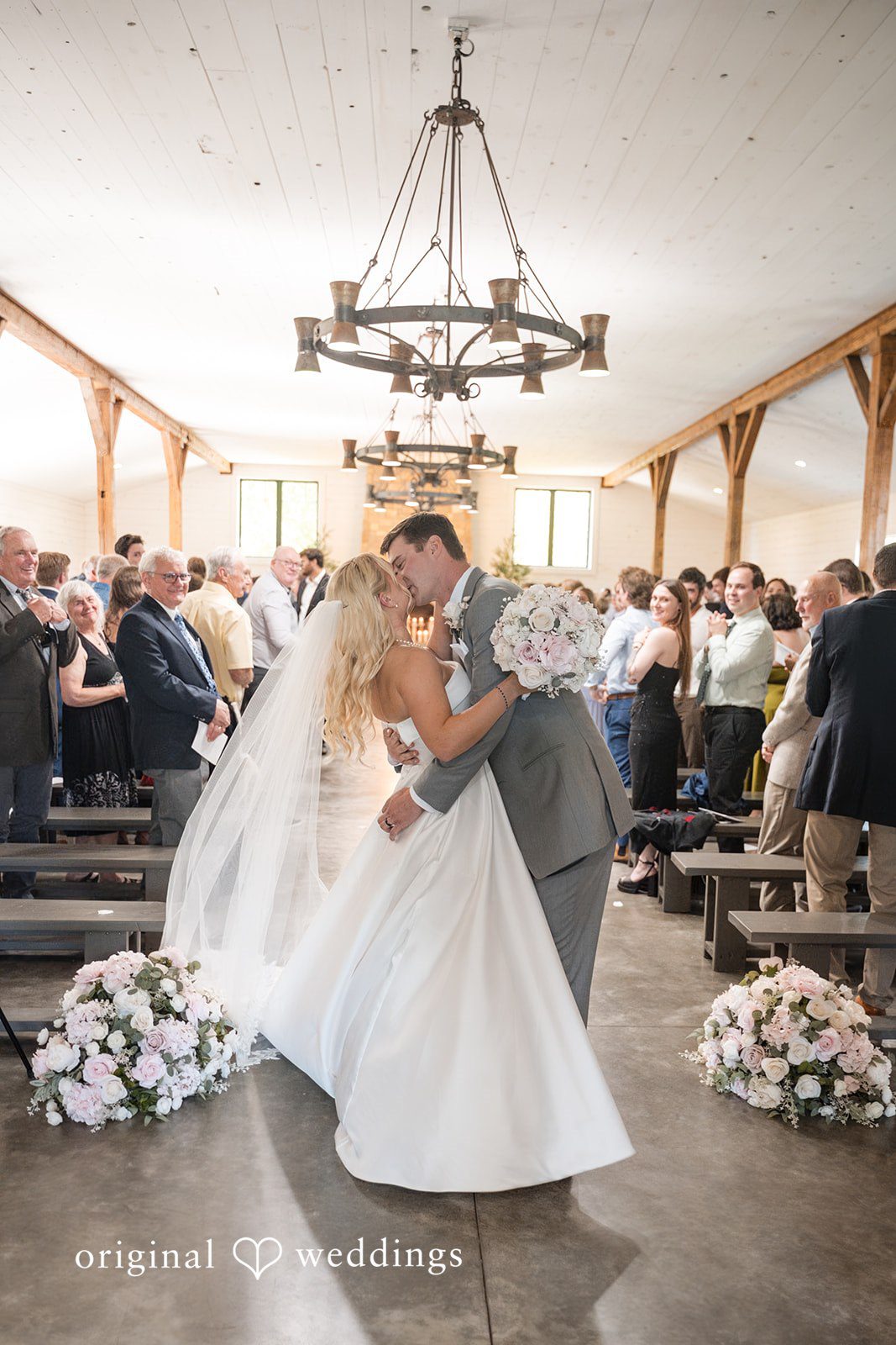 Cassandra + Adam Bride and groom sharing a kiss surrounded by wedding guests.