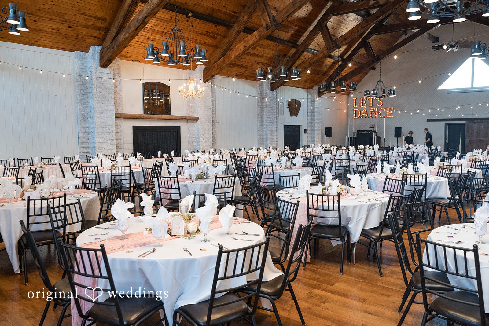 Cassandra + Adam Reception hall filled with round dining tables, chairs, and white tablecloths.