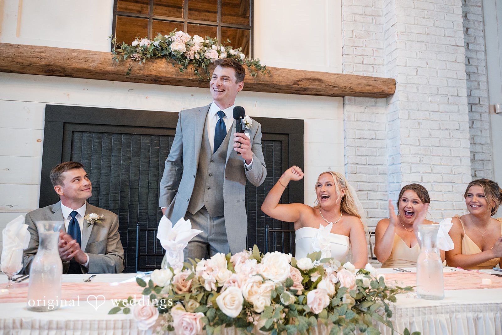 Cassandra + Adam Groom speaking into a microphone at the reception head table while guests listen.
