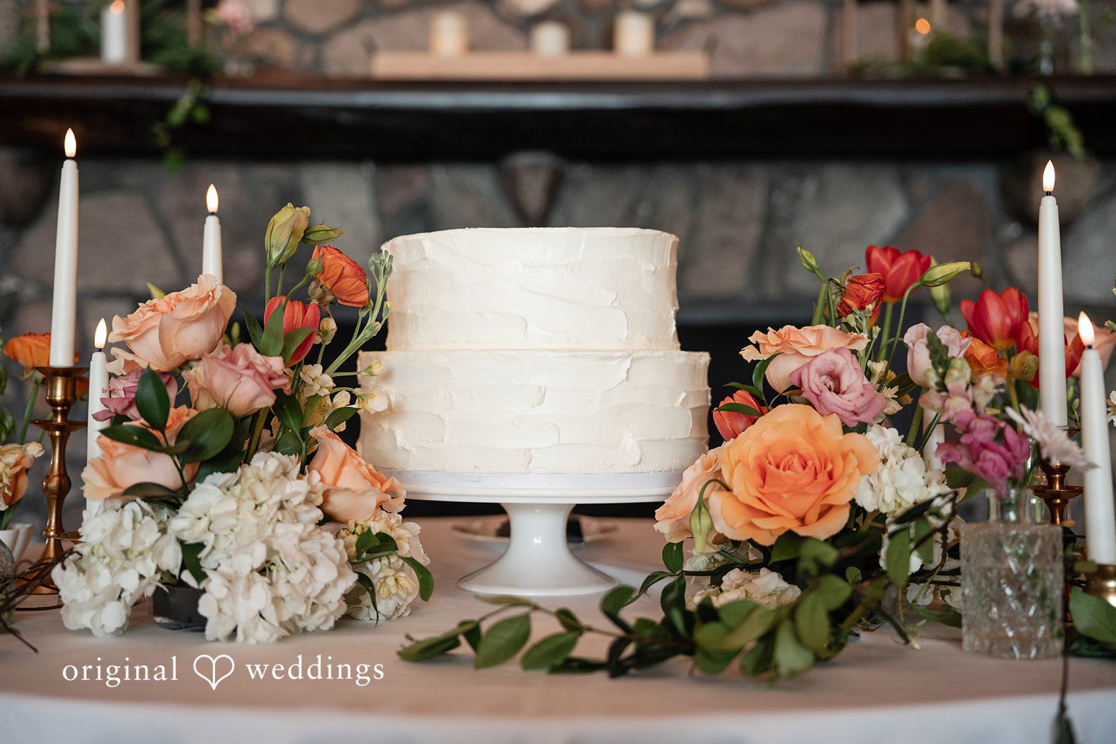 Annie + Andrew Beautiful white wedding cake placed in between flowers and candles