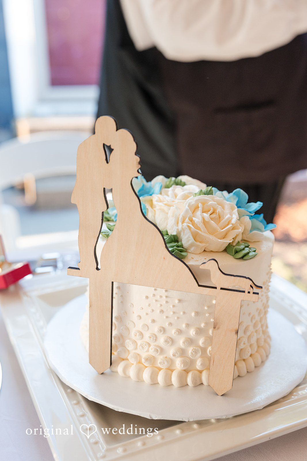 John + Emma A white frosted wedding cake topped with cream and blue flowers