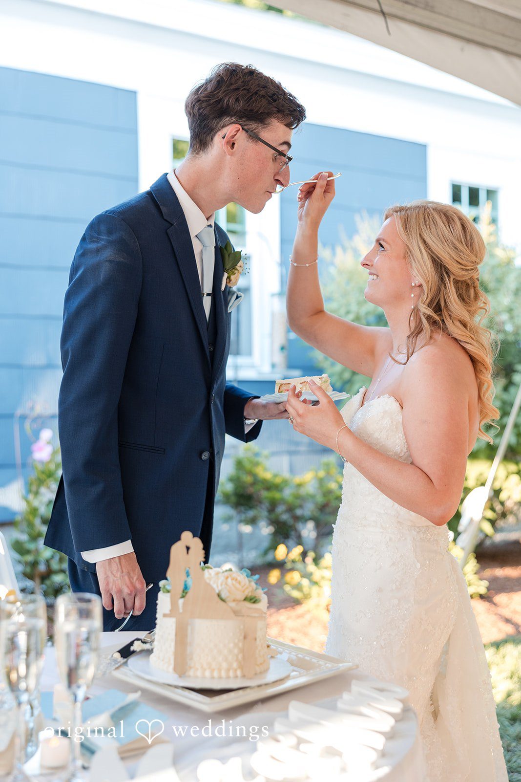 John + Emma Newlyweds playfully feeding each other wedding cake.