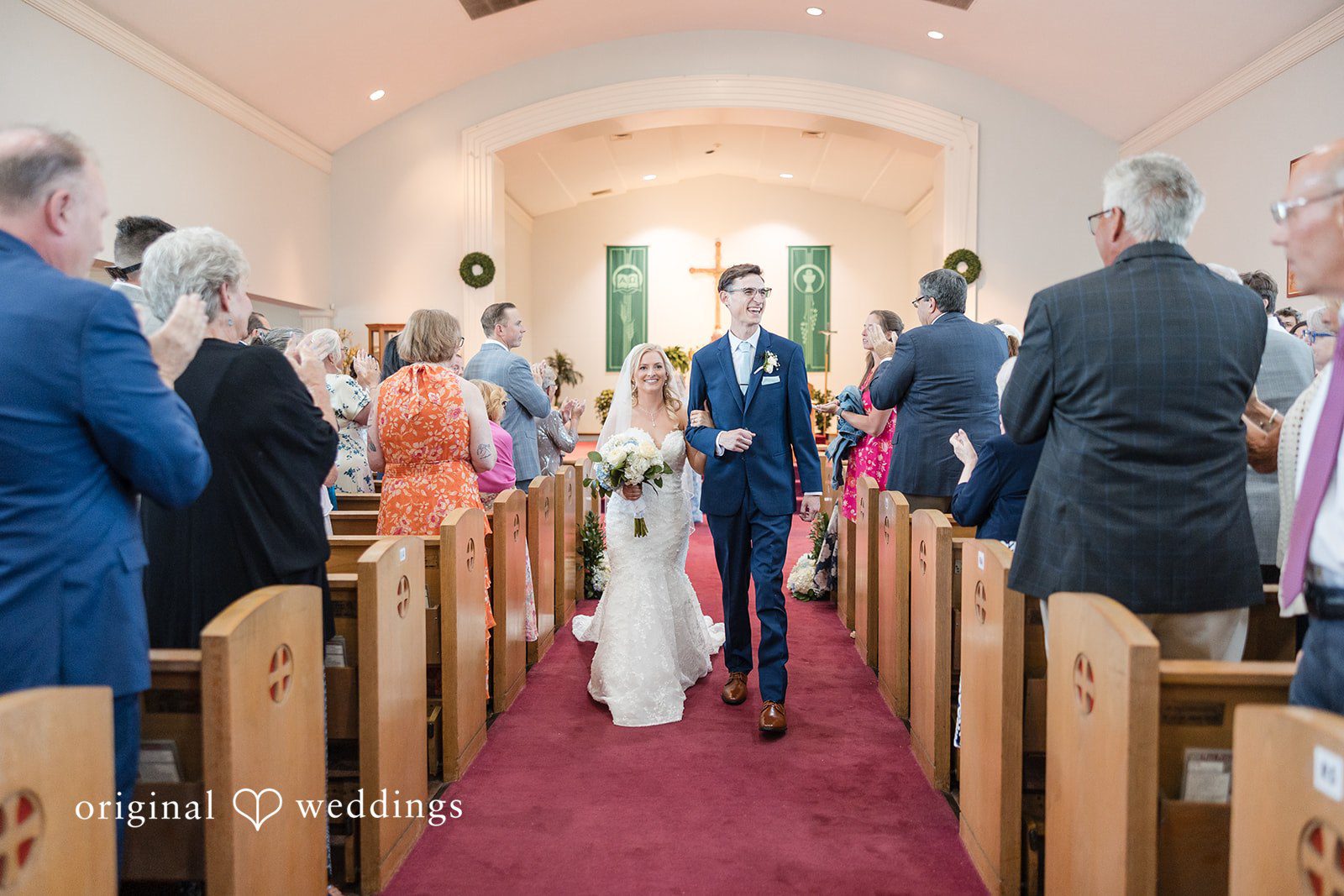John + Emma Newlyweds walking up the church aisle past cheering guests.