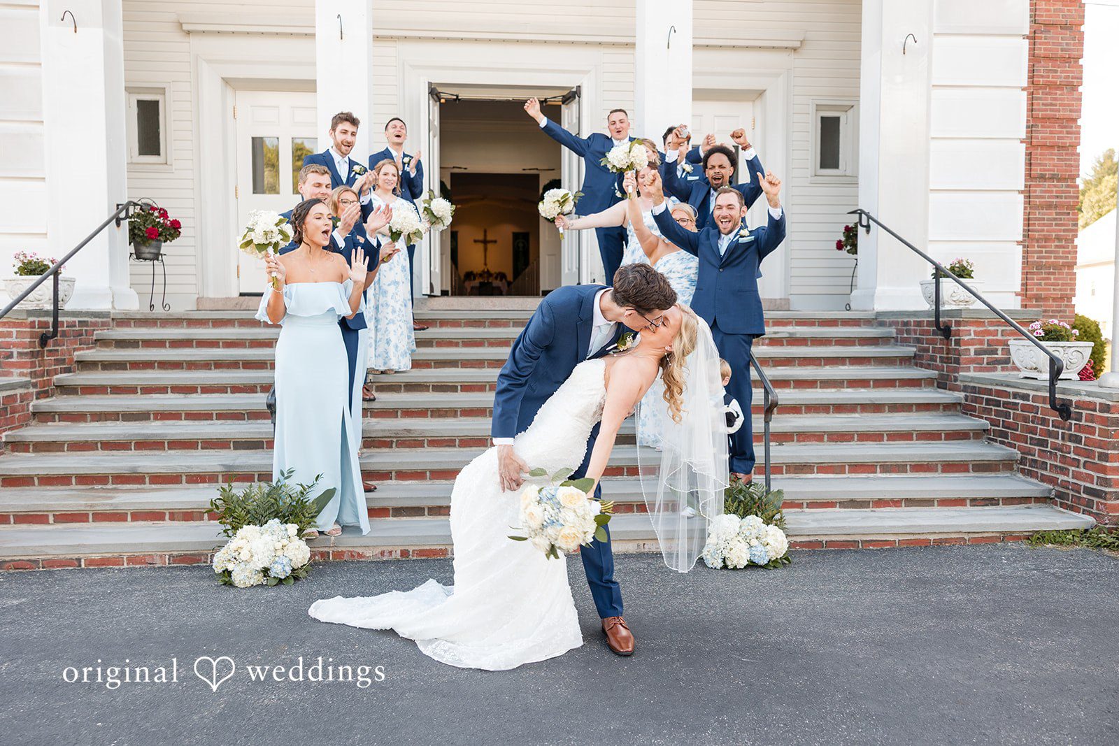 John + Emma Bride and groom kissing on steps while guests celebrate.