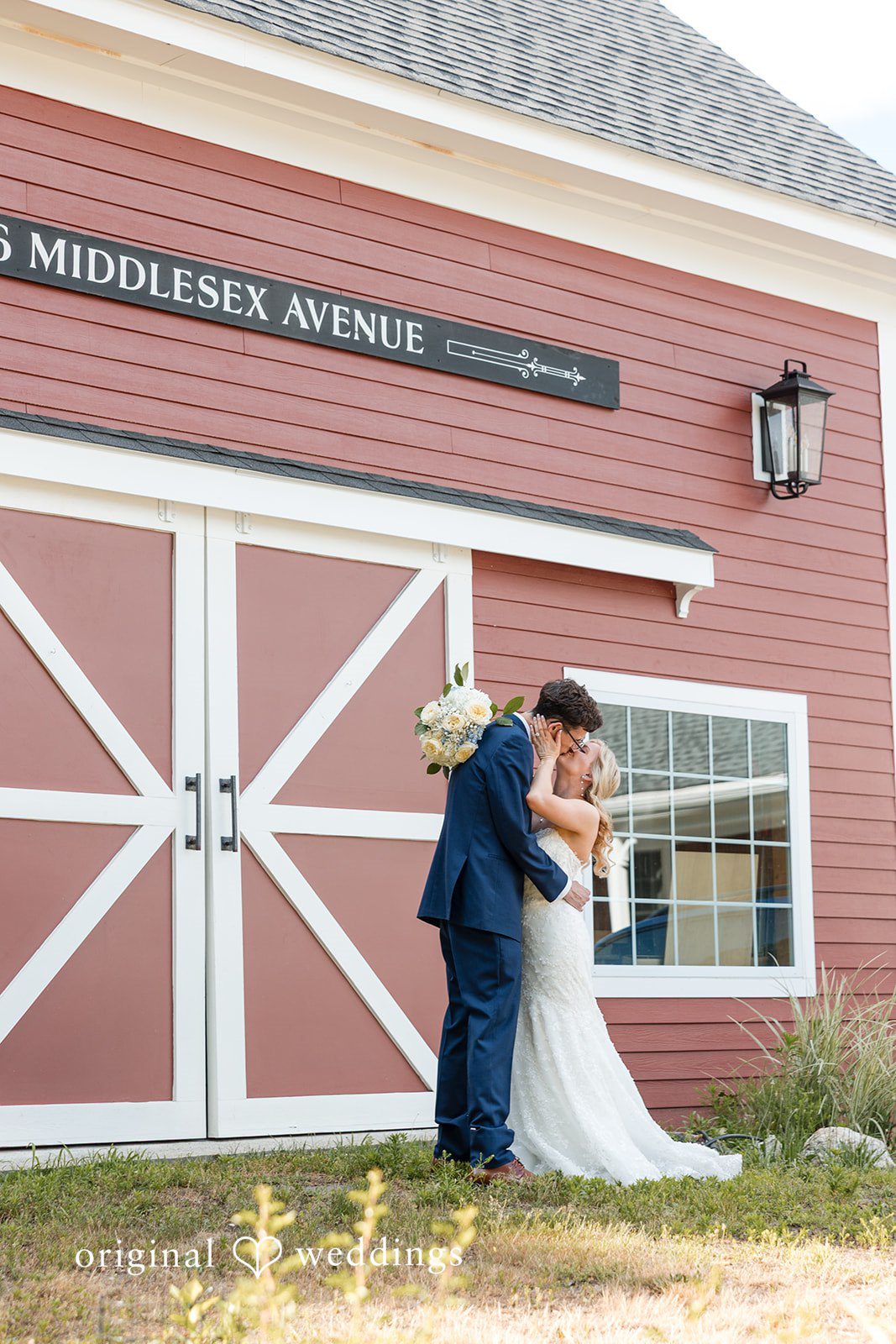 John + Emma Bride and groom embracing outside a red barn entrance.