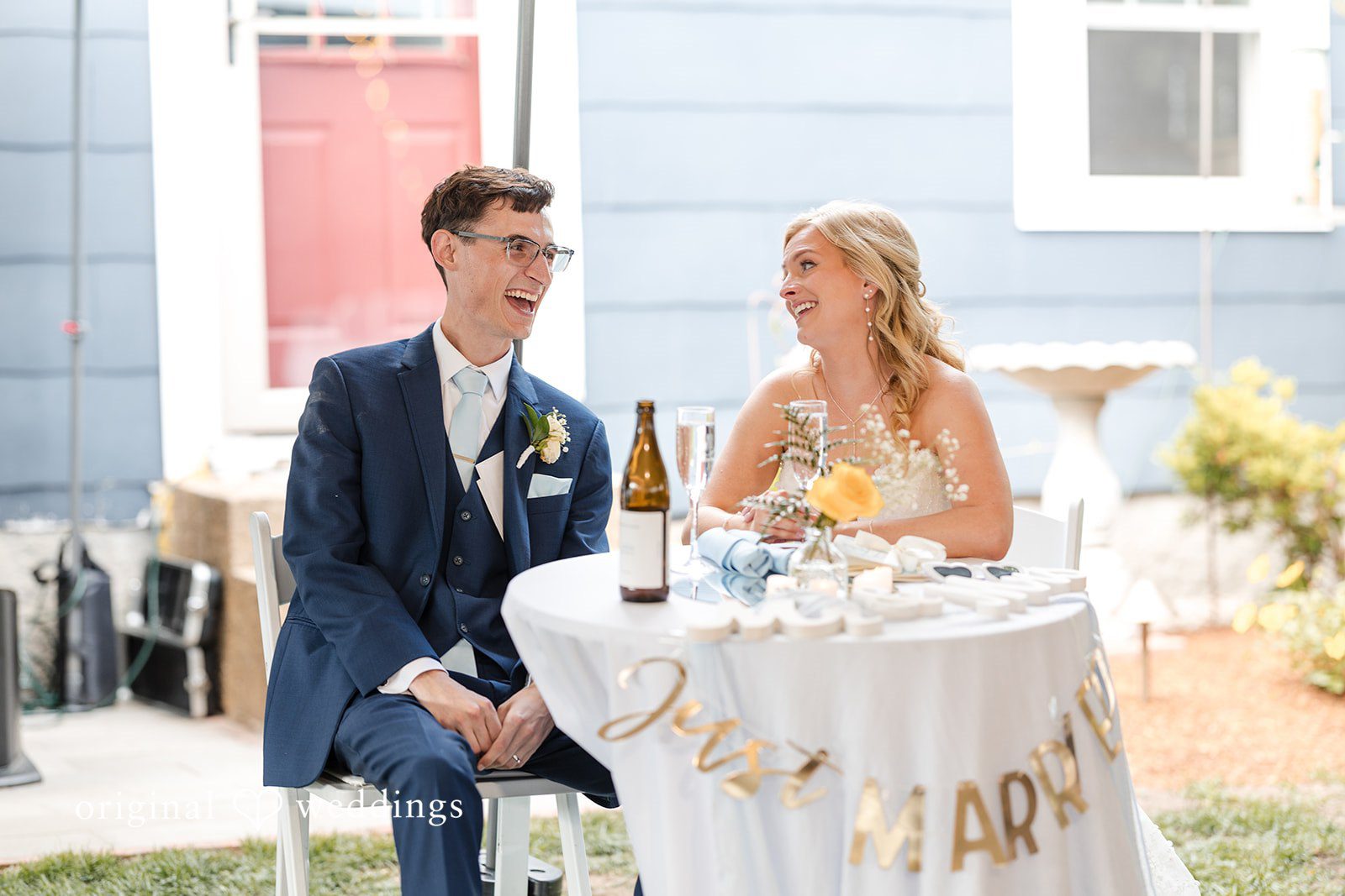John + Emma Bride and groom sitting at their decorated reception table.
