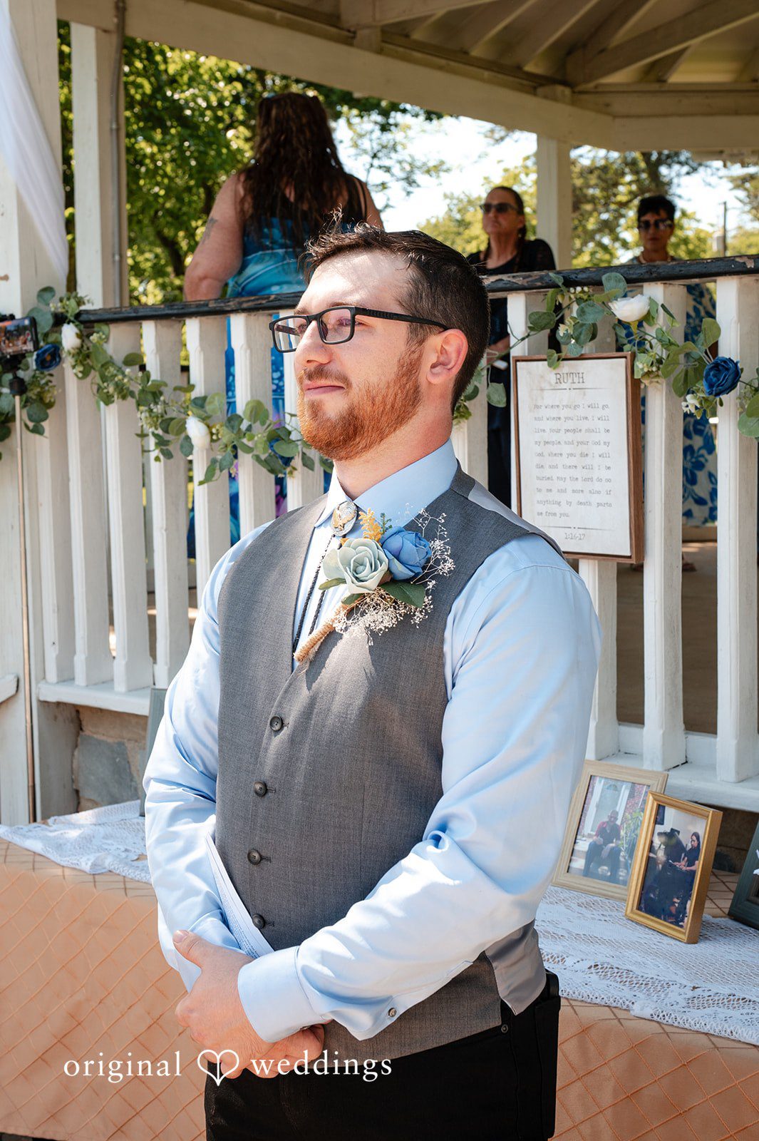 Joshua + Angela A groom with glasses wearing a grey vest, light blue shirt, and a floral boutonniere.