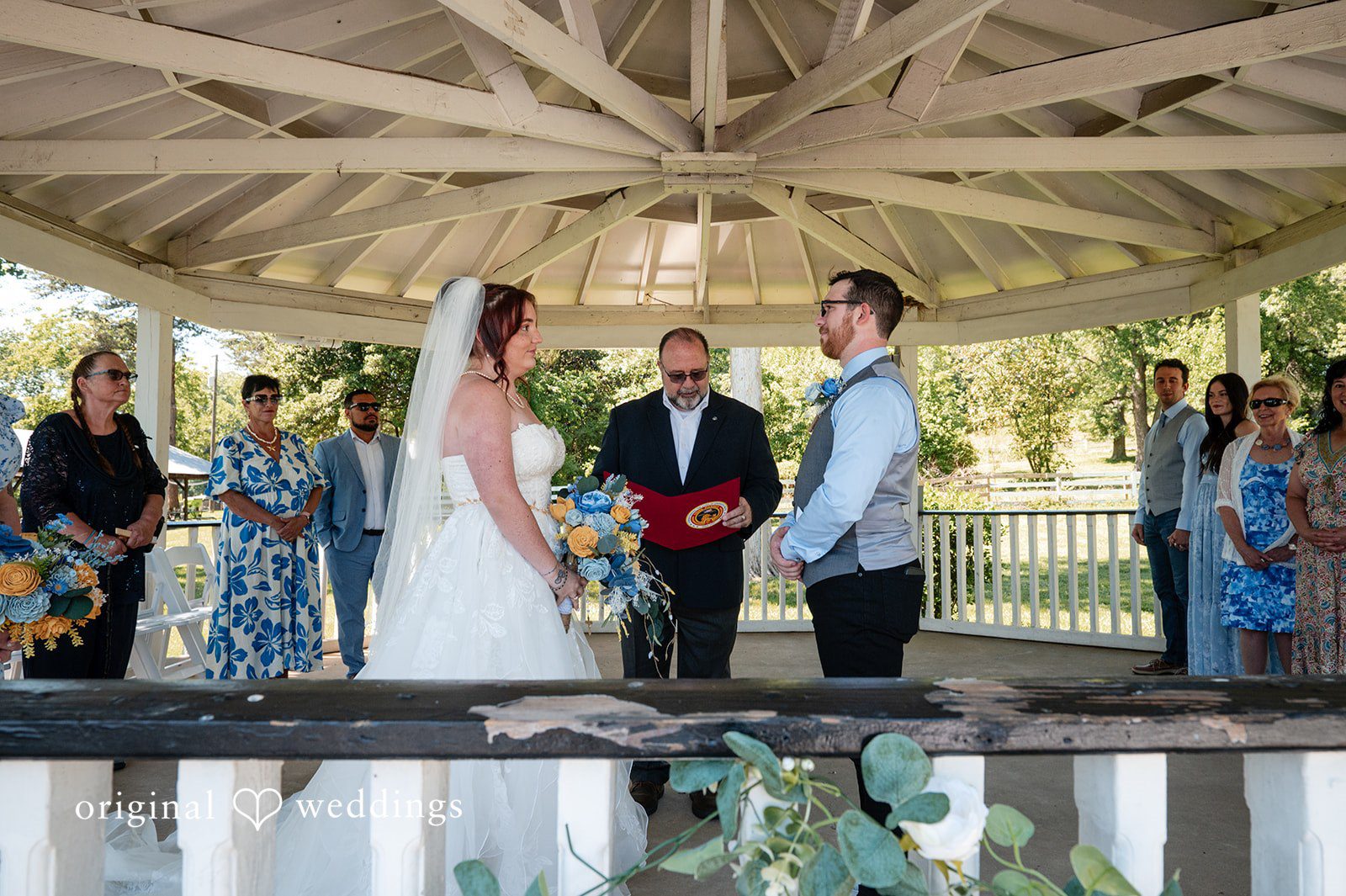 Joshua + Angela A bride and groom stand at the altar inside a white gazebo during their wedding ceremony.