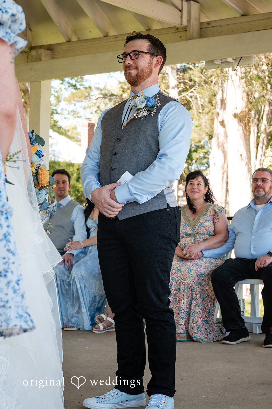 Joshua + Angela A groom with glasses and a grey vest looks happily toward his bride during the ceremony.