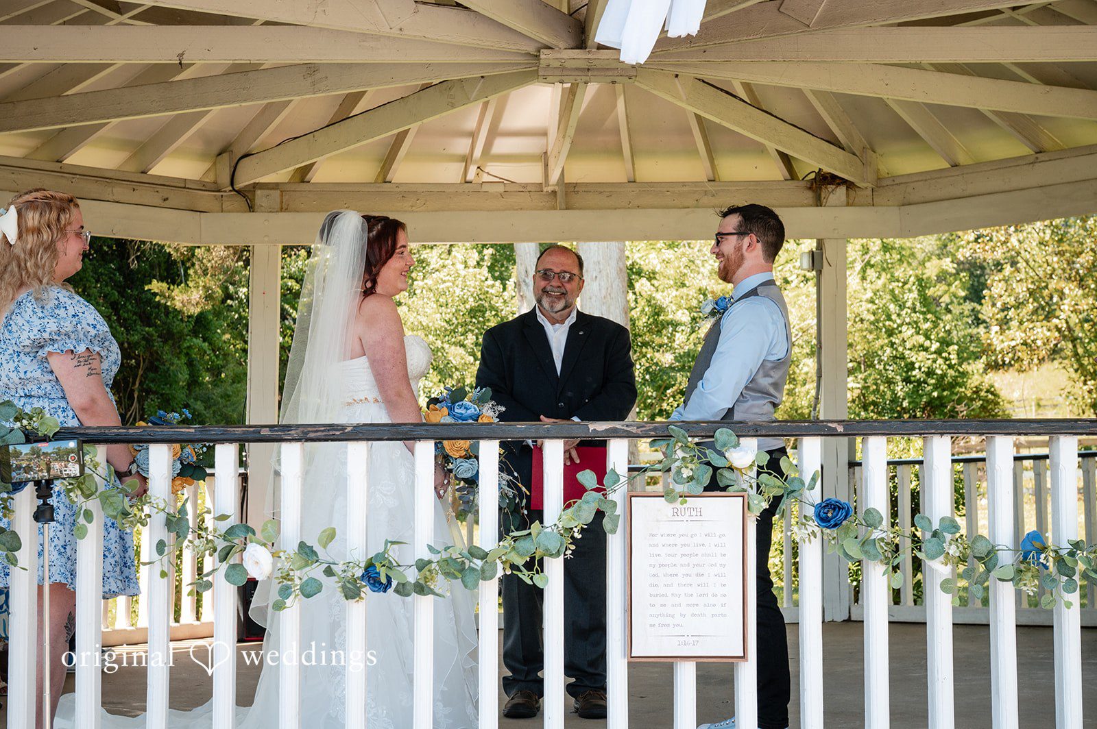 Joshua + Angela A wide shot of a wedding ceremony taking place inside a decorated white gazebo with an officiant.