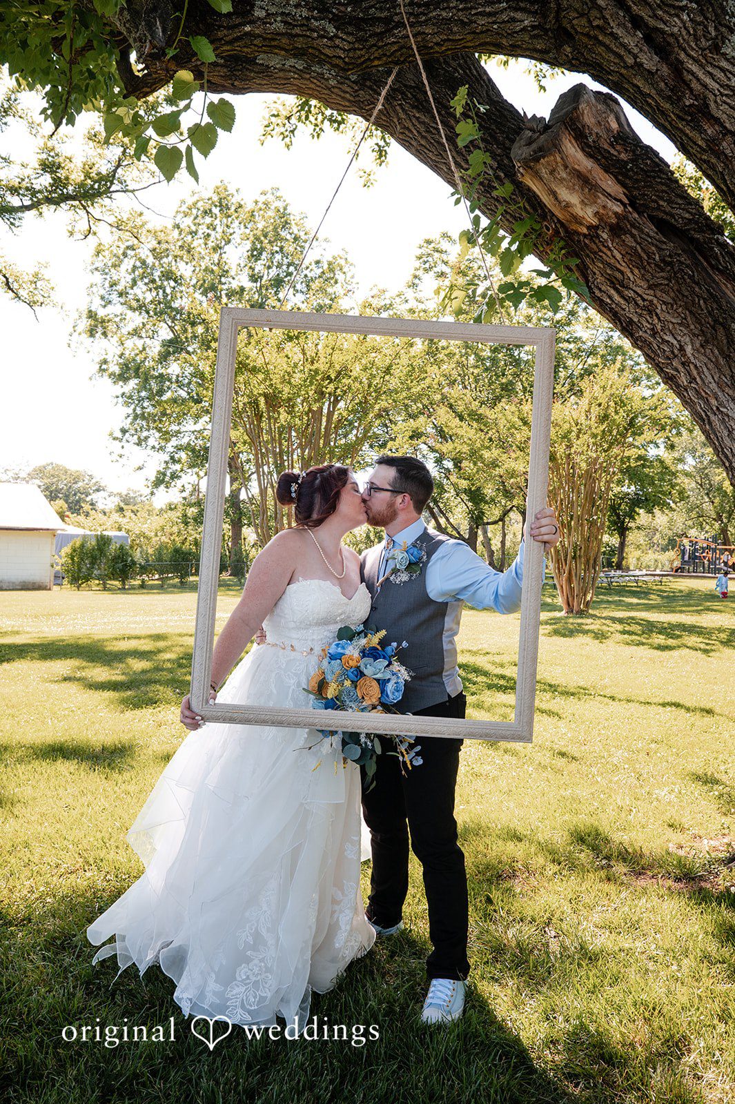 Joshua + Angela A bride and groom share a kiss while framing themselves inside a large rustic picture frame outdoors.