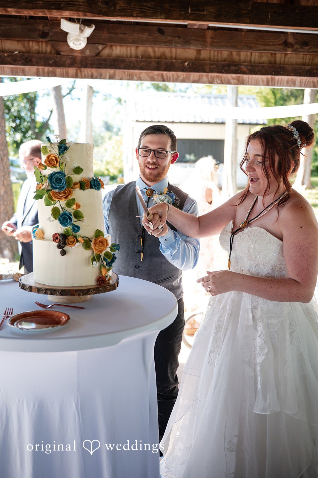 Joshua + Angela A bride and groom smiling as they prepare to cut their multi-tiered wedding cake.