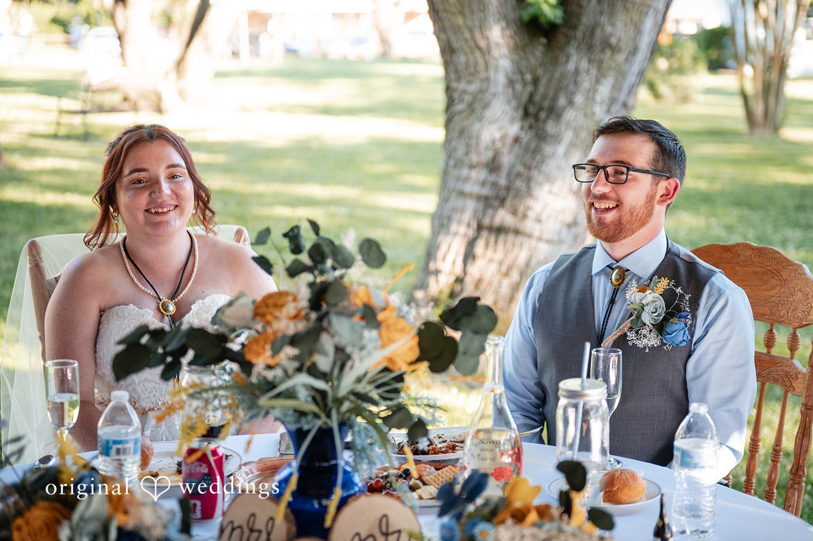 Joshua + Angela A bride and groom sitting at their decorated head table during the wedding reception.