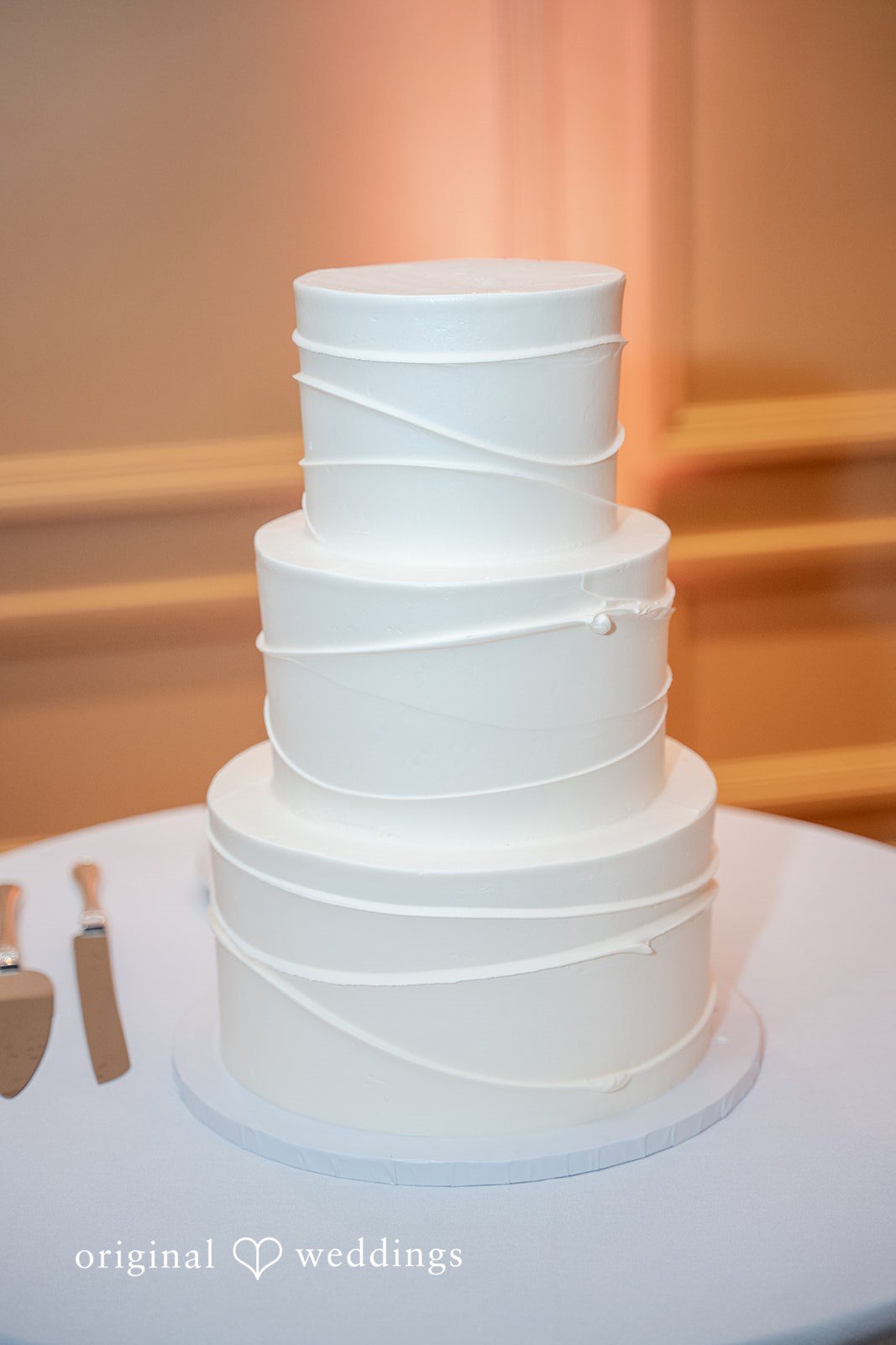 Aislyn + Alex Three-tiered white wedding cake with smooth frosting on a stand.