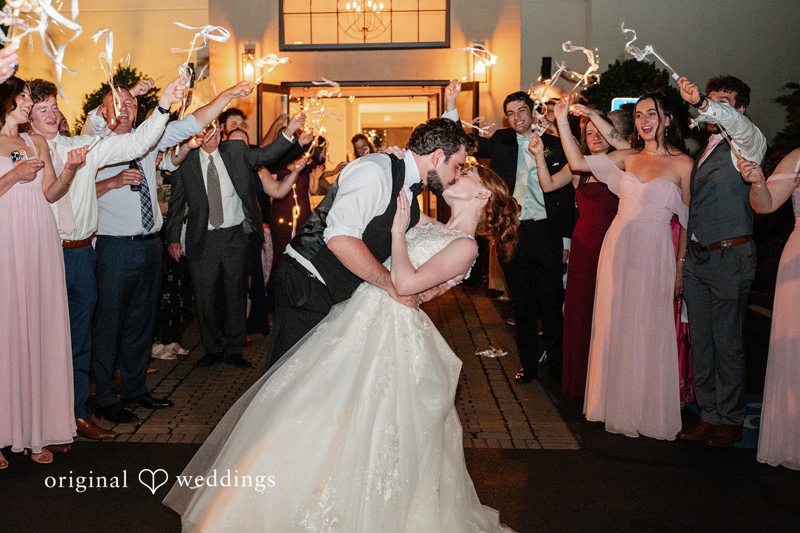 Aislyn + Alex Bride and groom sharing a dip kiss on the dance floor surrounded by cheering guests.