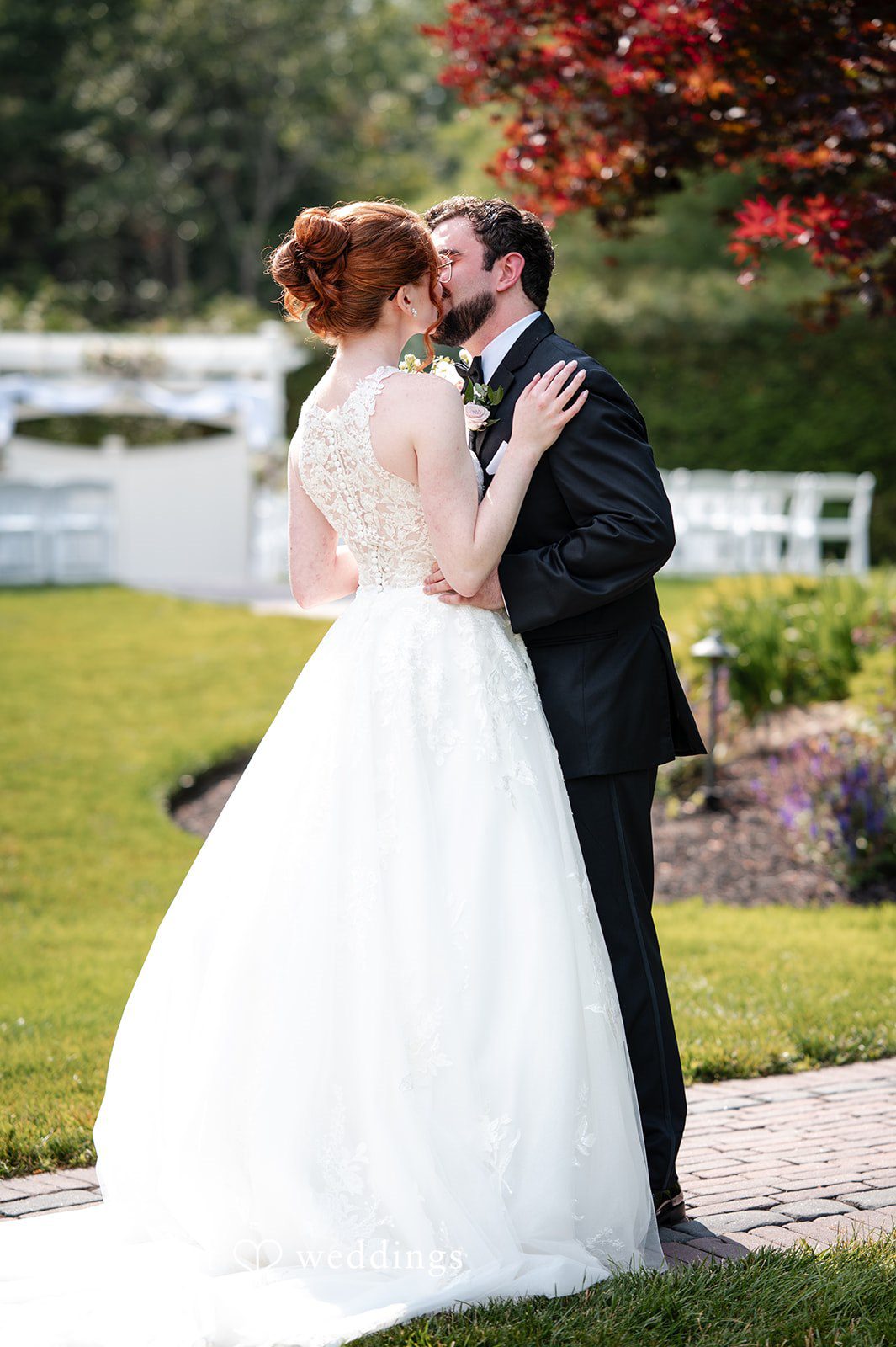 Aislyn + Alex Groom embracing the bride from behind on a lawn.