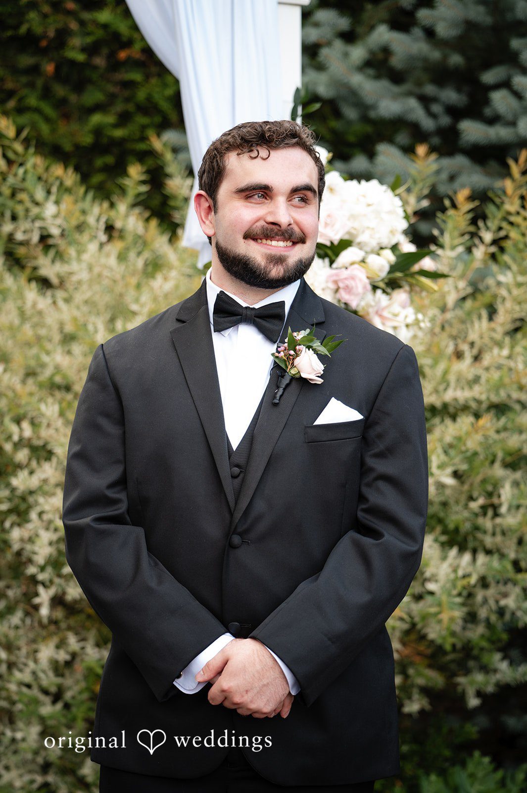 Aislyn + Alex Portrait of a groom smiling in a black tuxedo with a floral boutonniere.