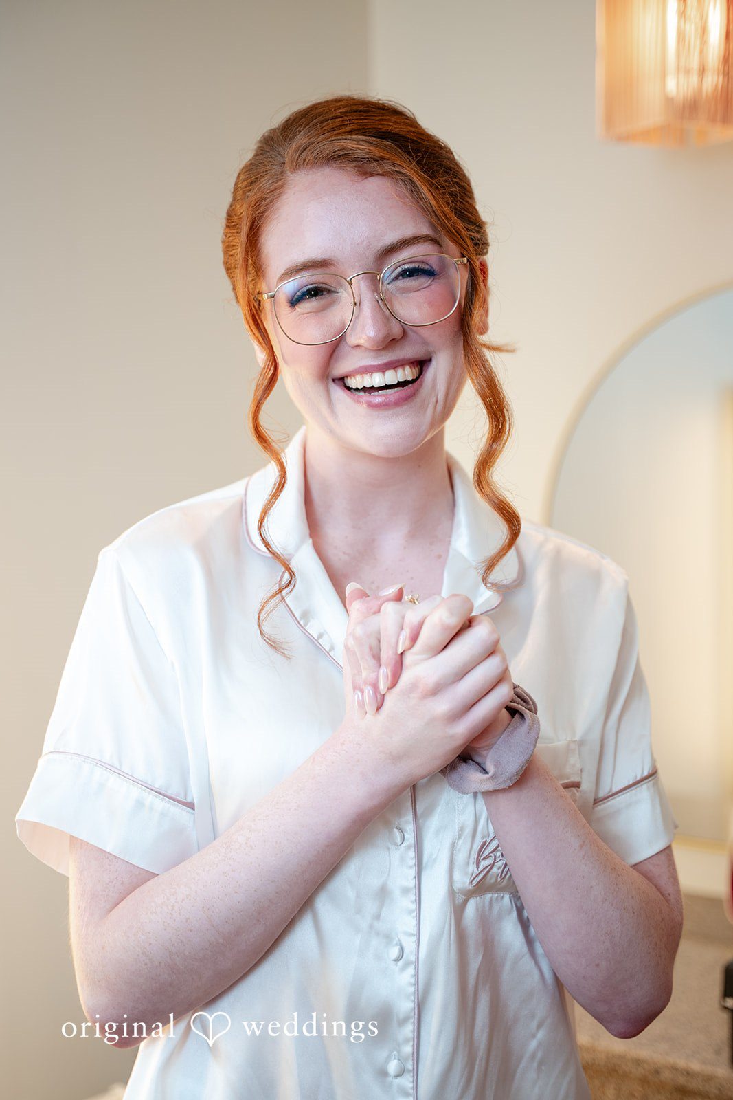 Aislyn + Alex Smiling bride wearing a white silk pajama top, looking at the camera.