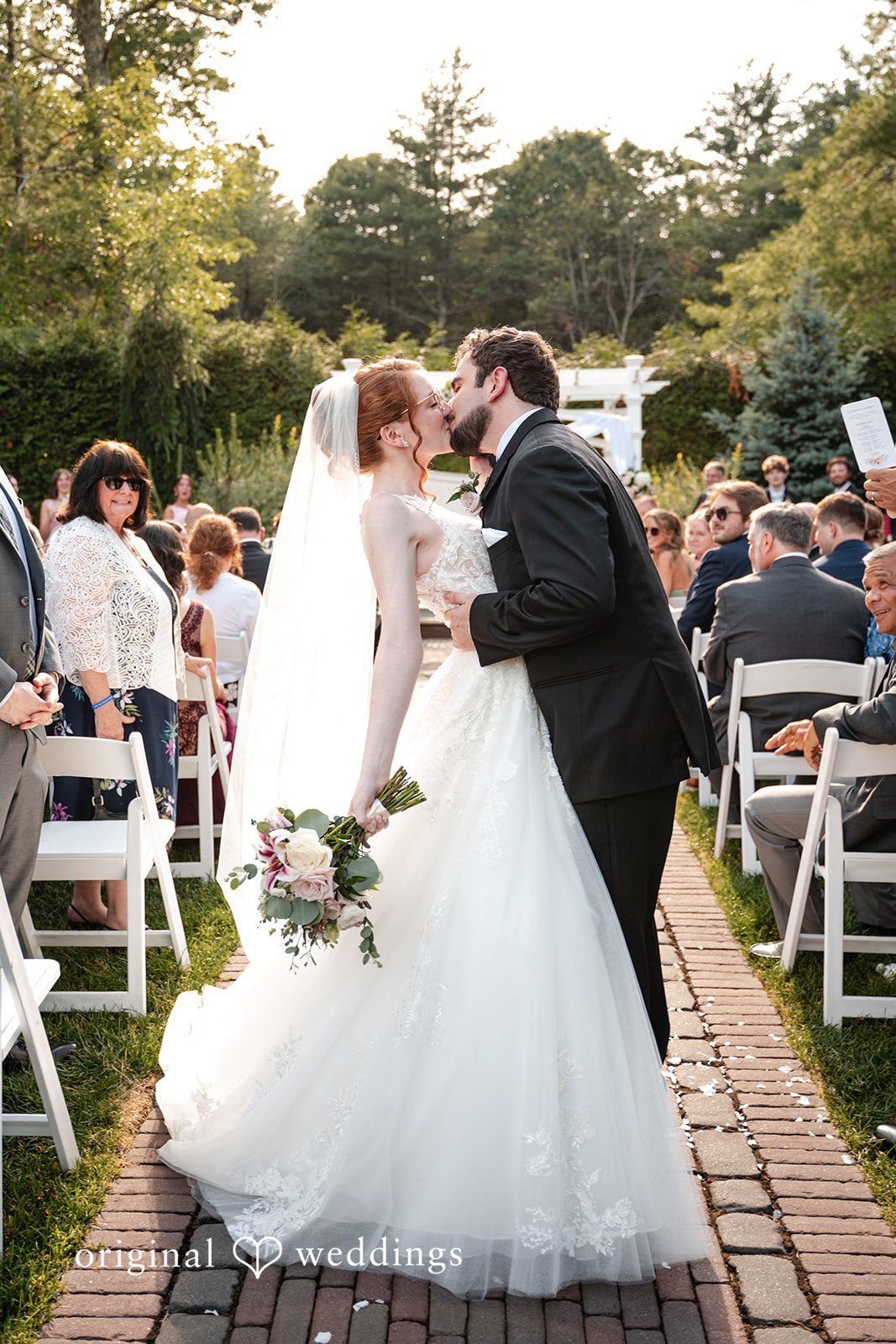 Aislyn + Alex Bride and groom kissing on the aisle while guests celebrate around them.