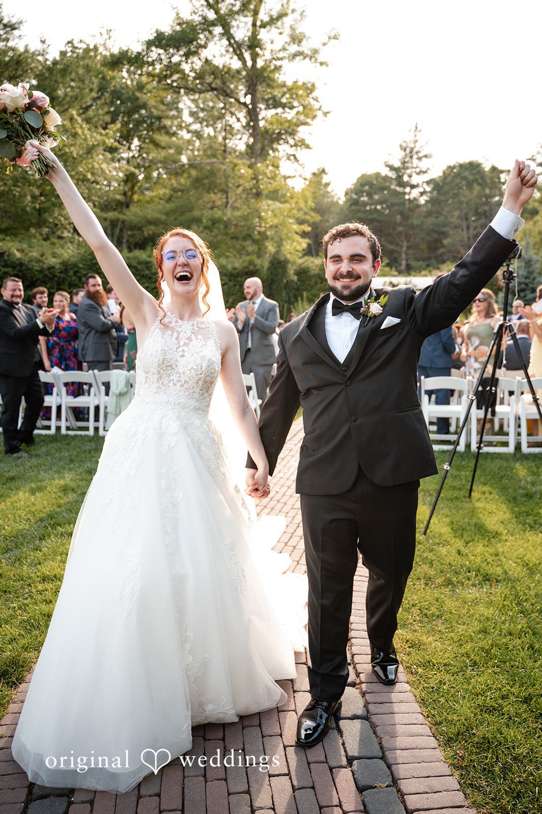 Aislyn + Alex Happy bride and groom cheering with raised hands while walking down the aisle.