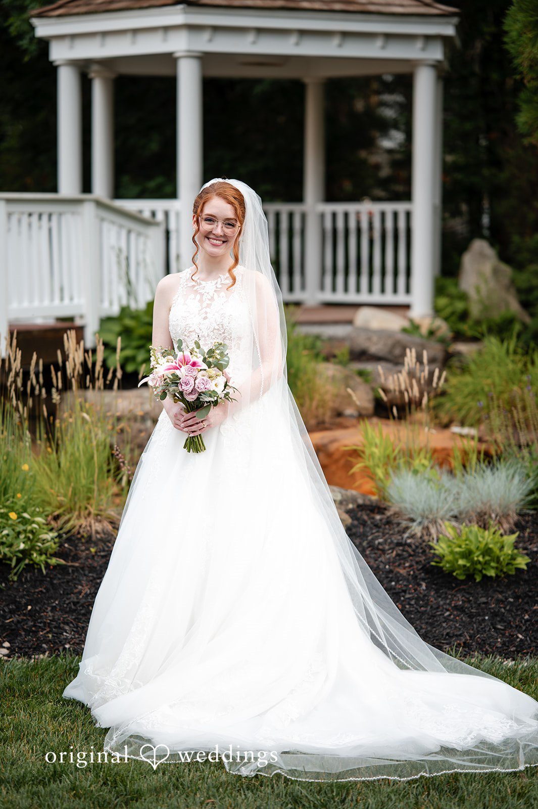 Aislyn + Alex Bride in a full white wedding gown and veil posing on a landscaped lawn.